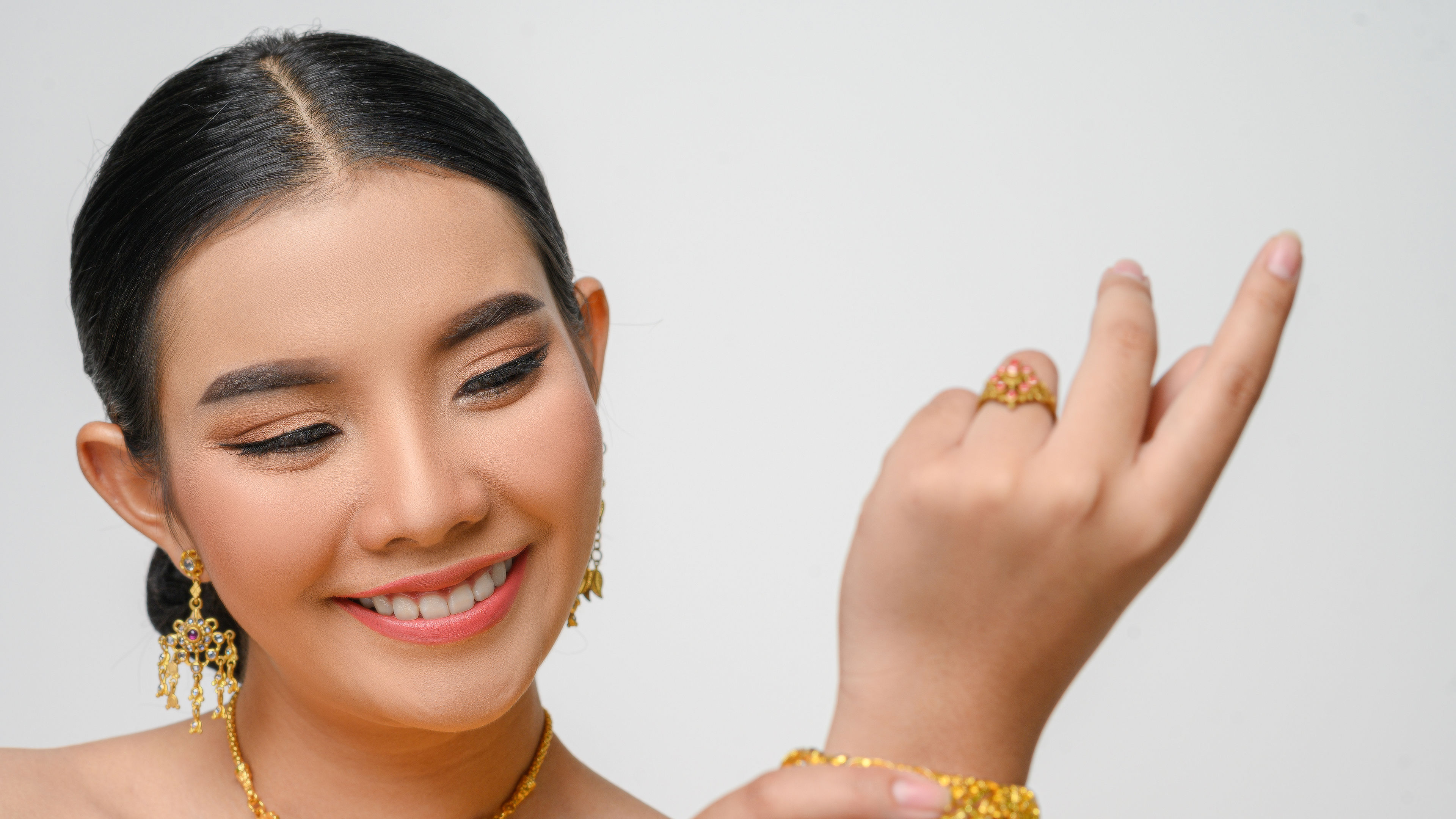 Beautiful Asian woman in traditional Thai dress costume wearing gold bangles in a white background.