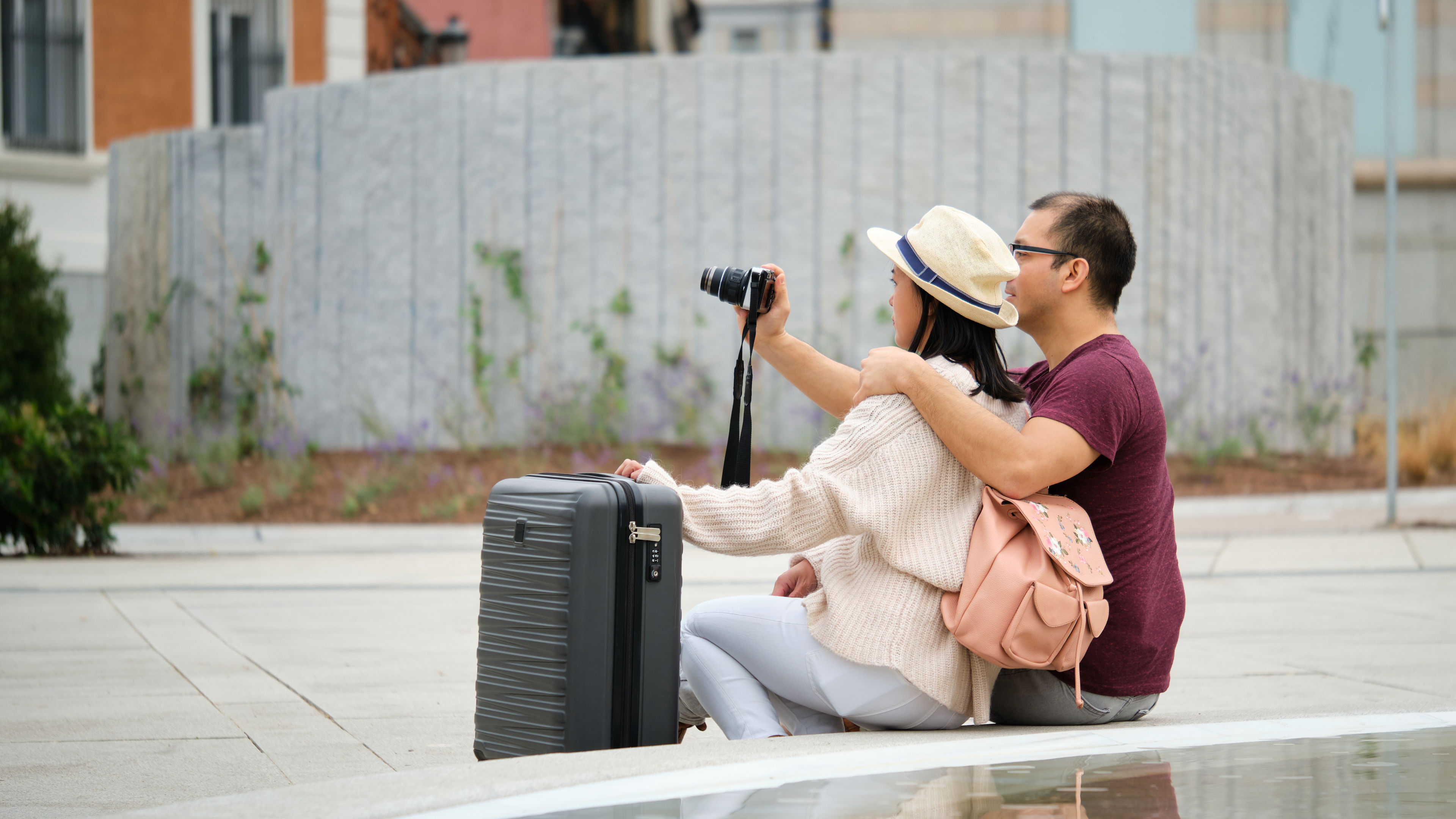 A couple is sitting near a fountain with their suitcase