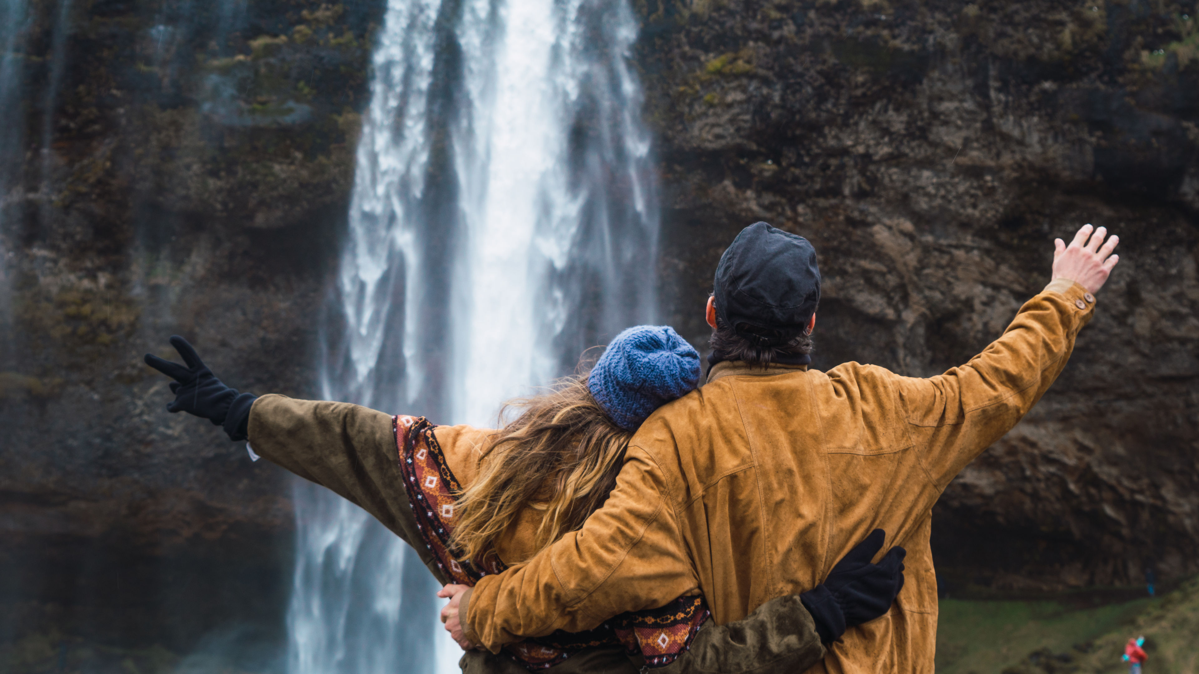 A couple stands close together at a waterfall