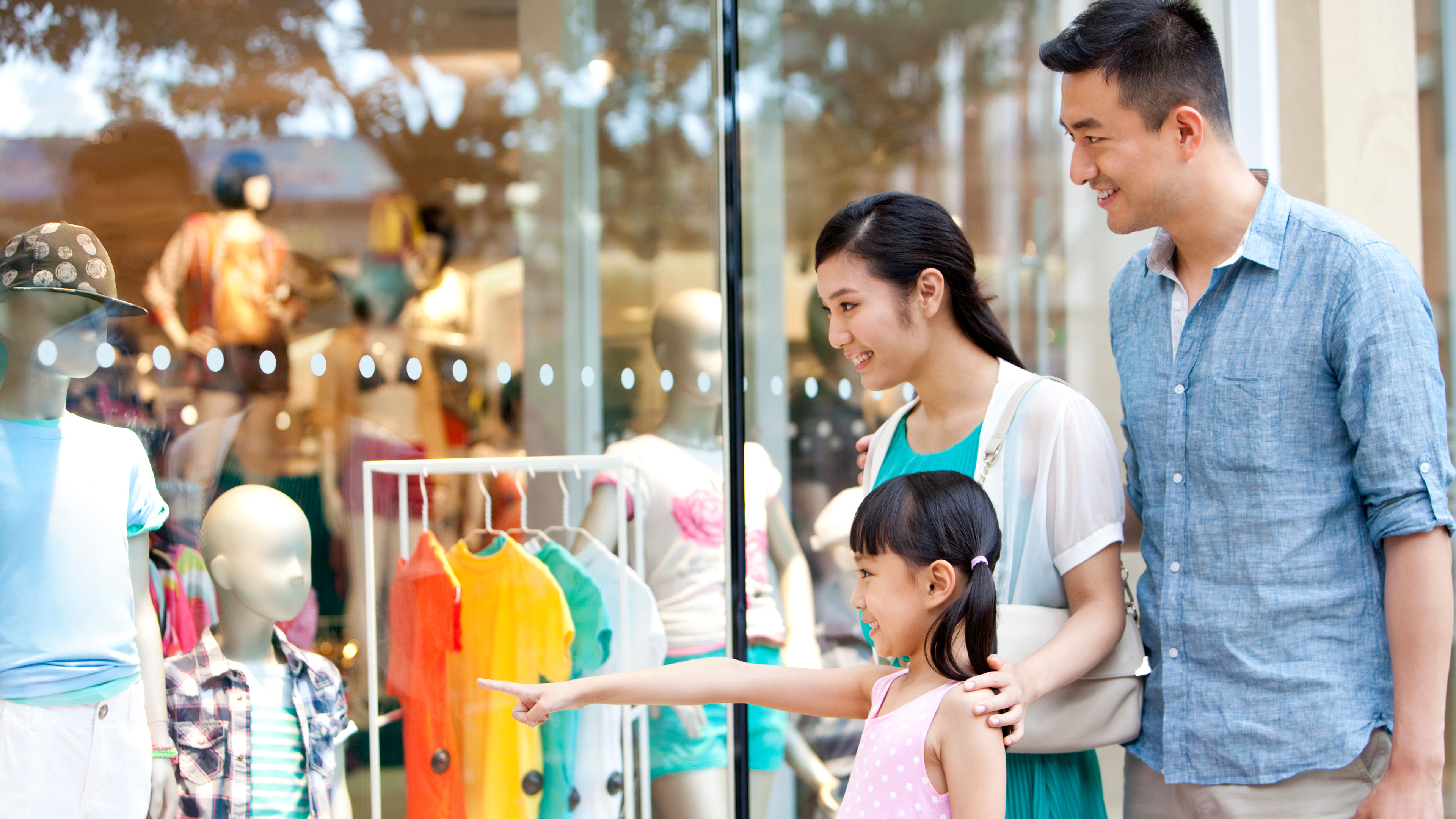 Parents and their daughter enjoy a delightful shopping trip, excitedly pointing at colorful outfits 
