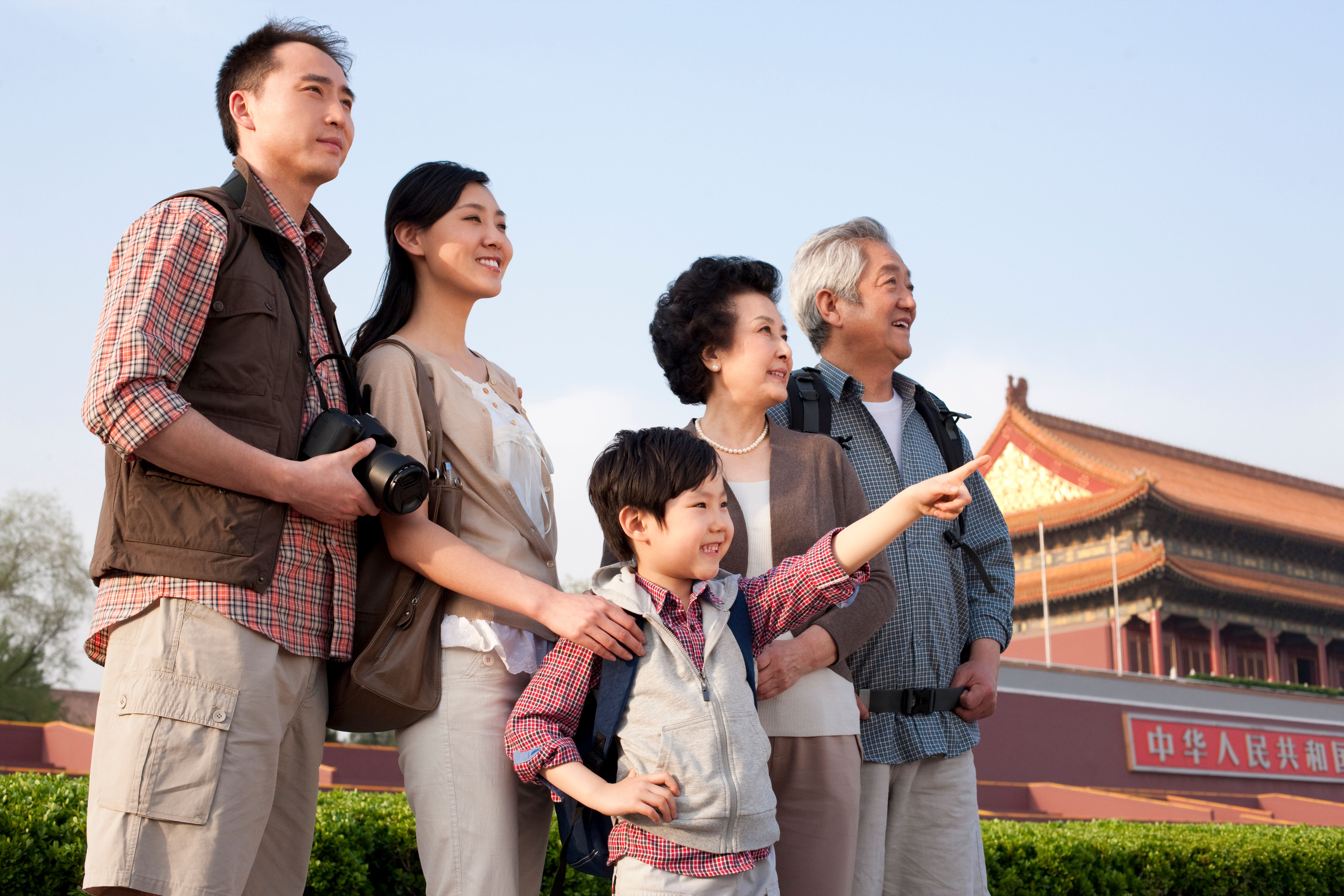 A joyful multi-generational family stands together at Tiananmen Square, the child pointing excitedly 