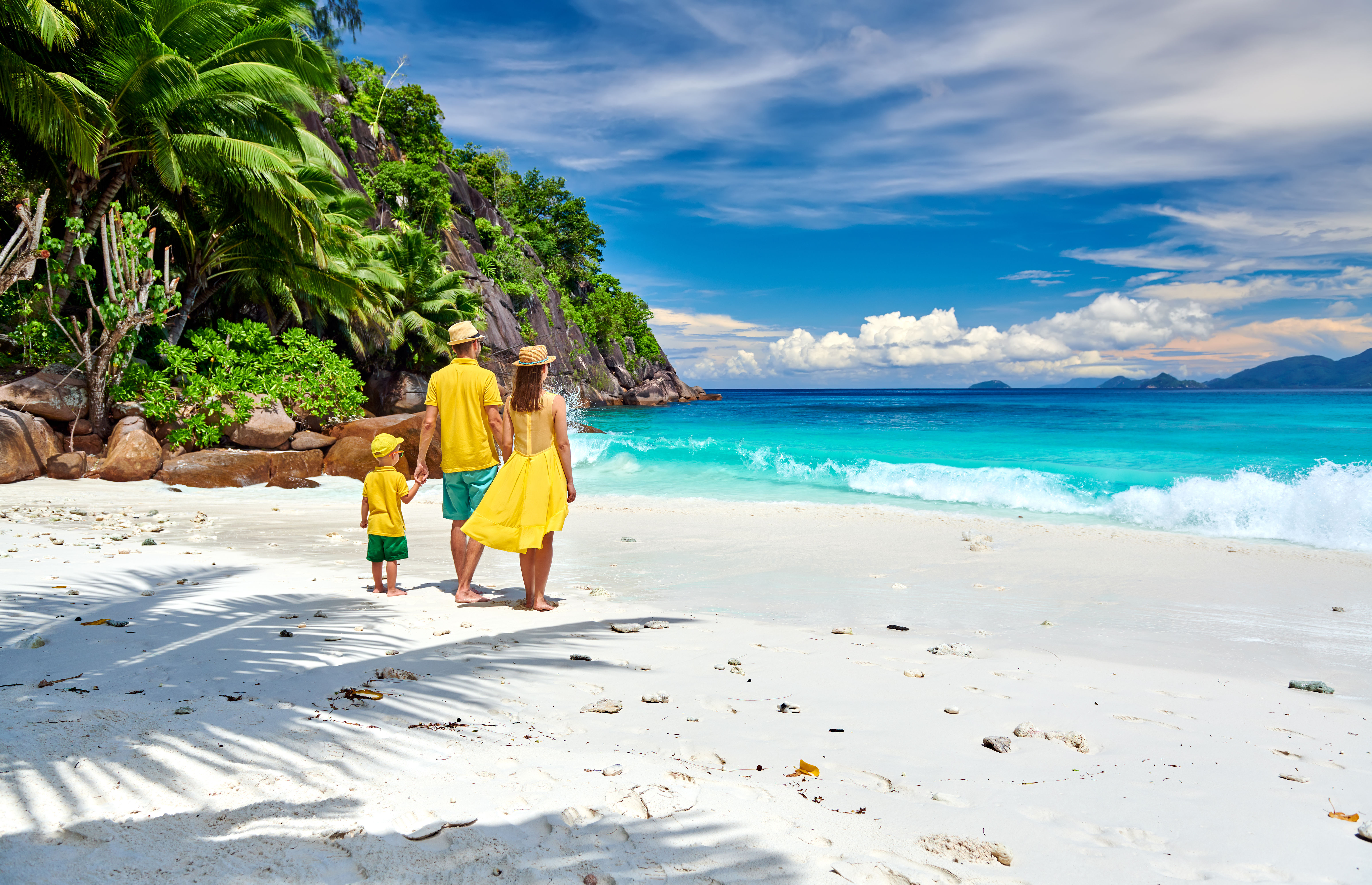 A family walks hand-in-hand along a white sandy beach