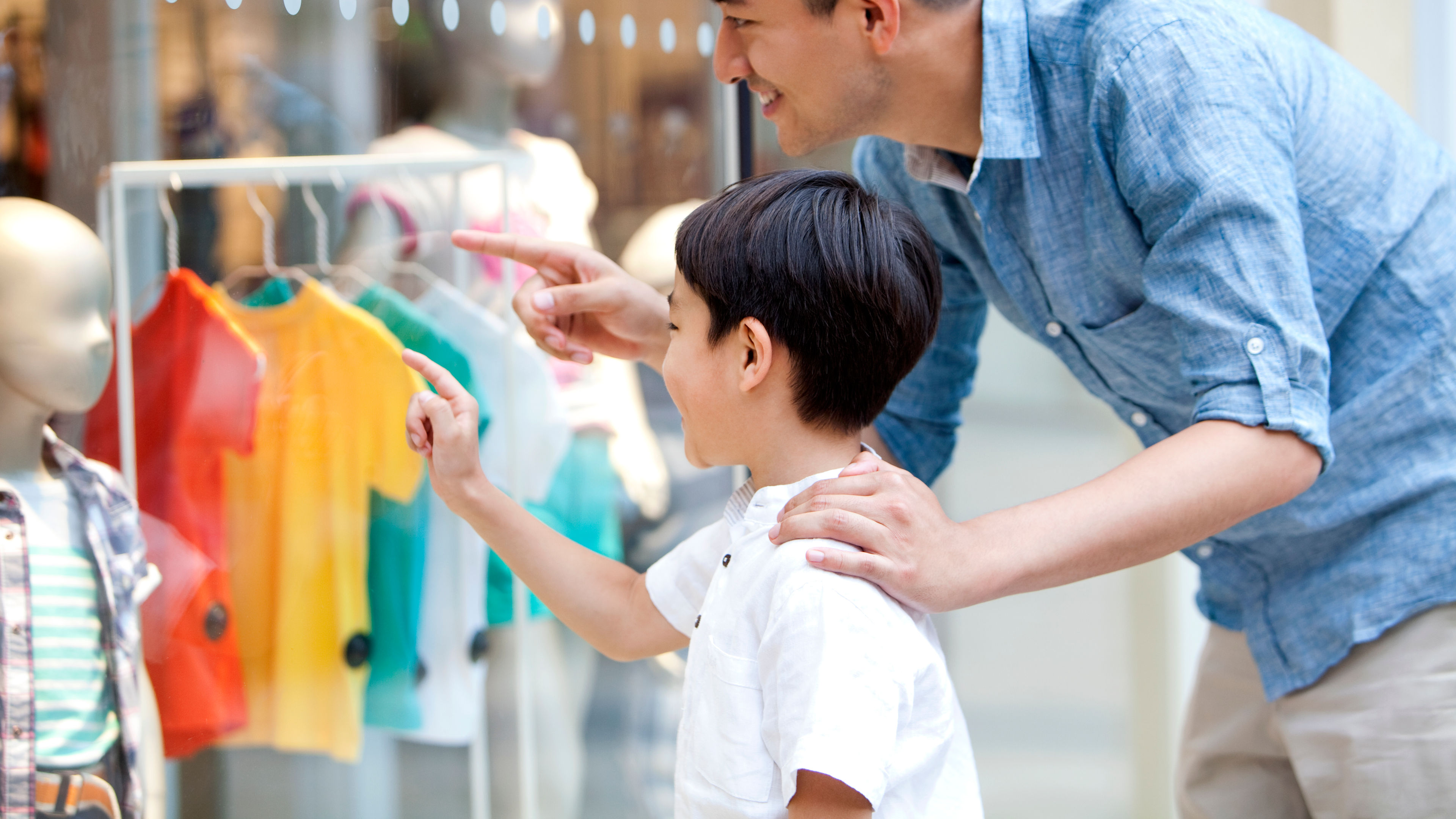 Father and son shares a joyful moment as they explore colorful outfits displayed in the shop’s window together. 