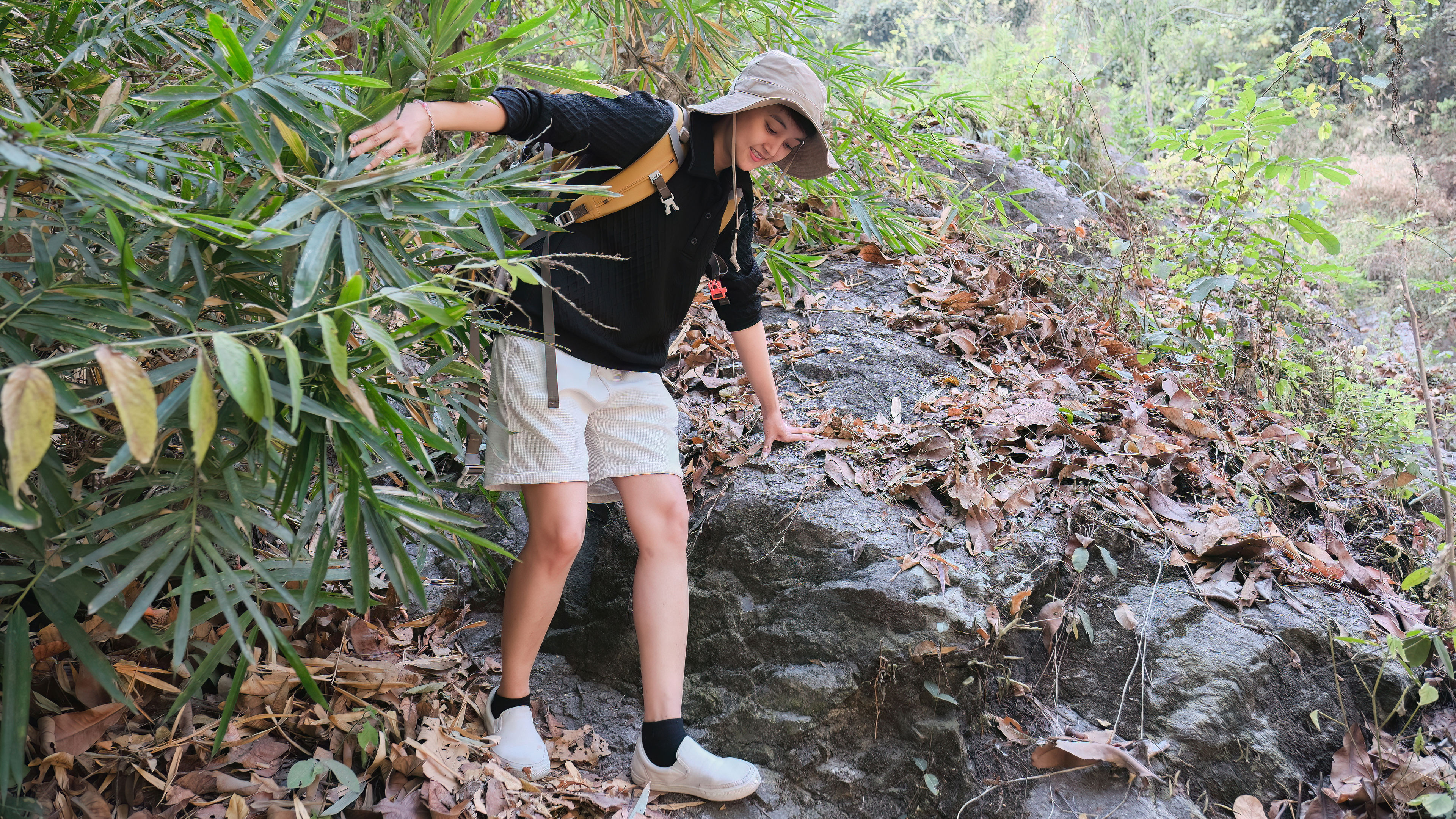 Wearing a sun hat and backpack, a woman carefully navigates a rocky forest path 