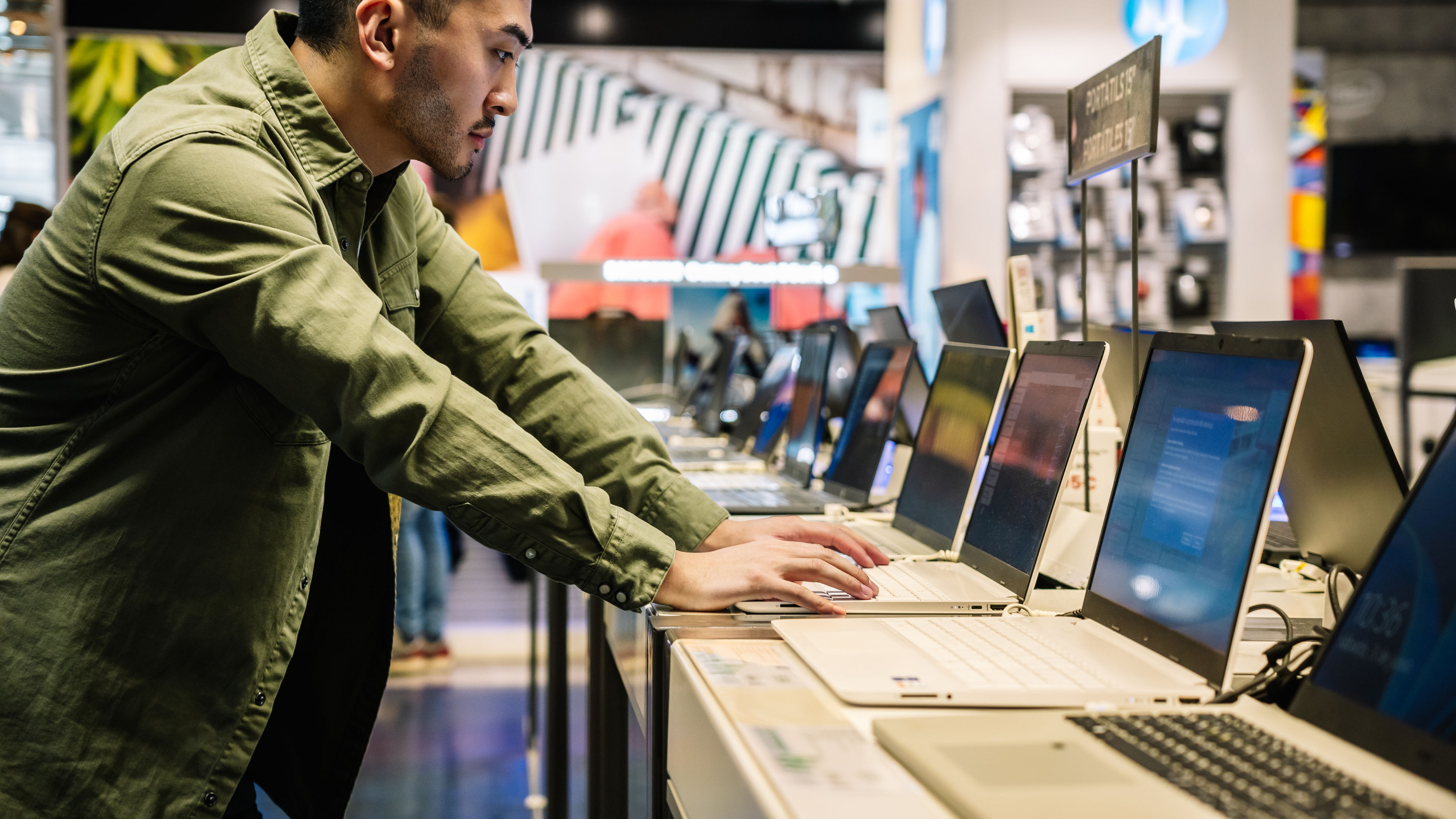 A man chooses laptops by checking their features in a shop. 