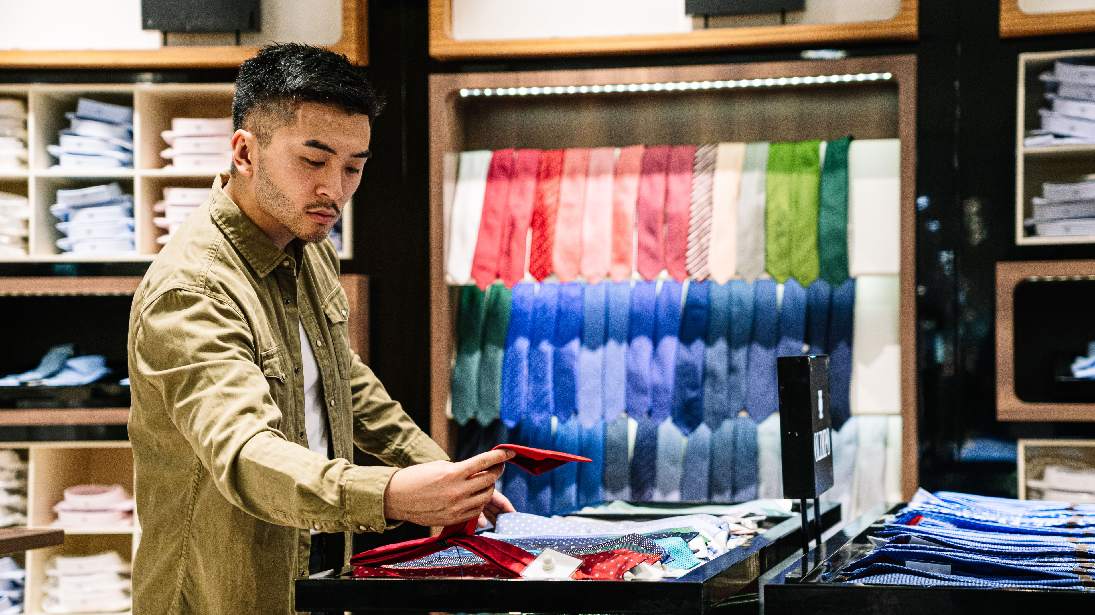 A man comparing various necktie designs and colors at a clothing shop. 