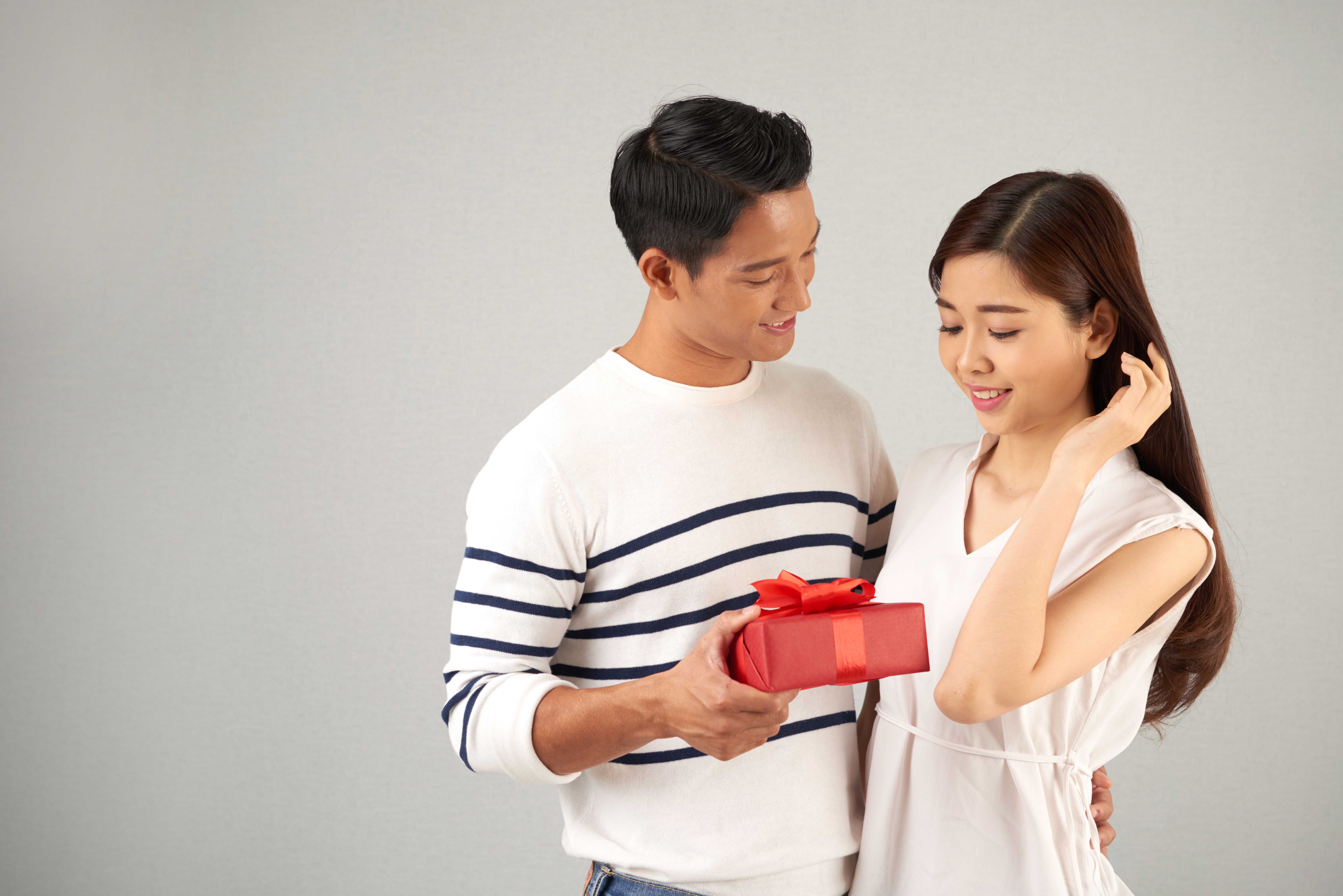 A cheerful man presents a beautifully wrapped red gift box to a smiling woman 
