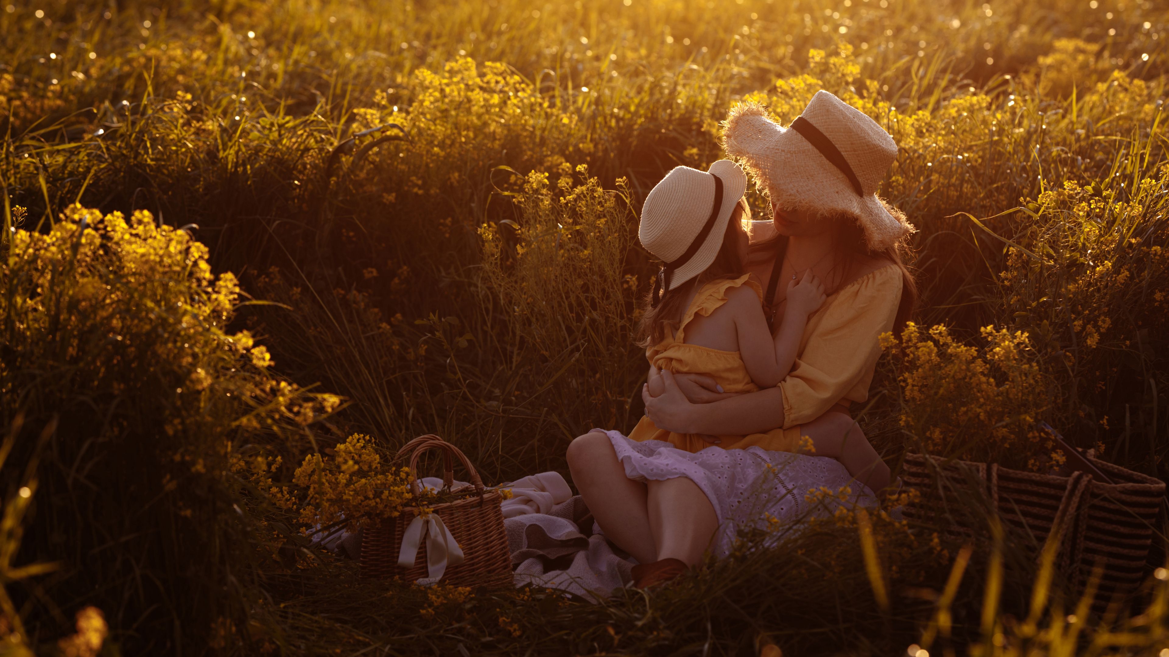A mother and daughter sit in a field full of yellow flowers.