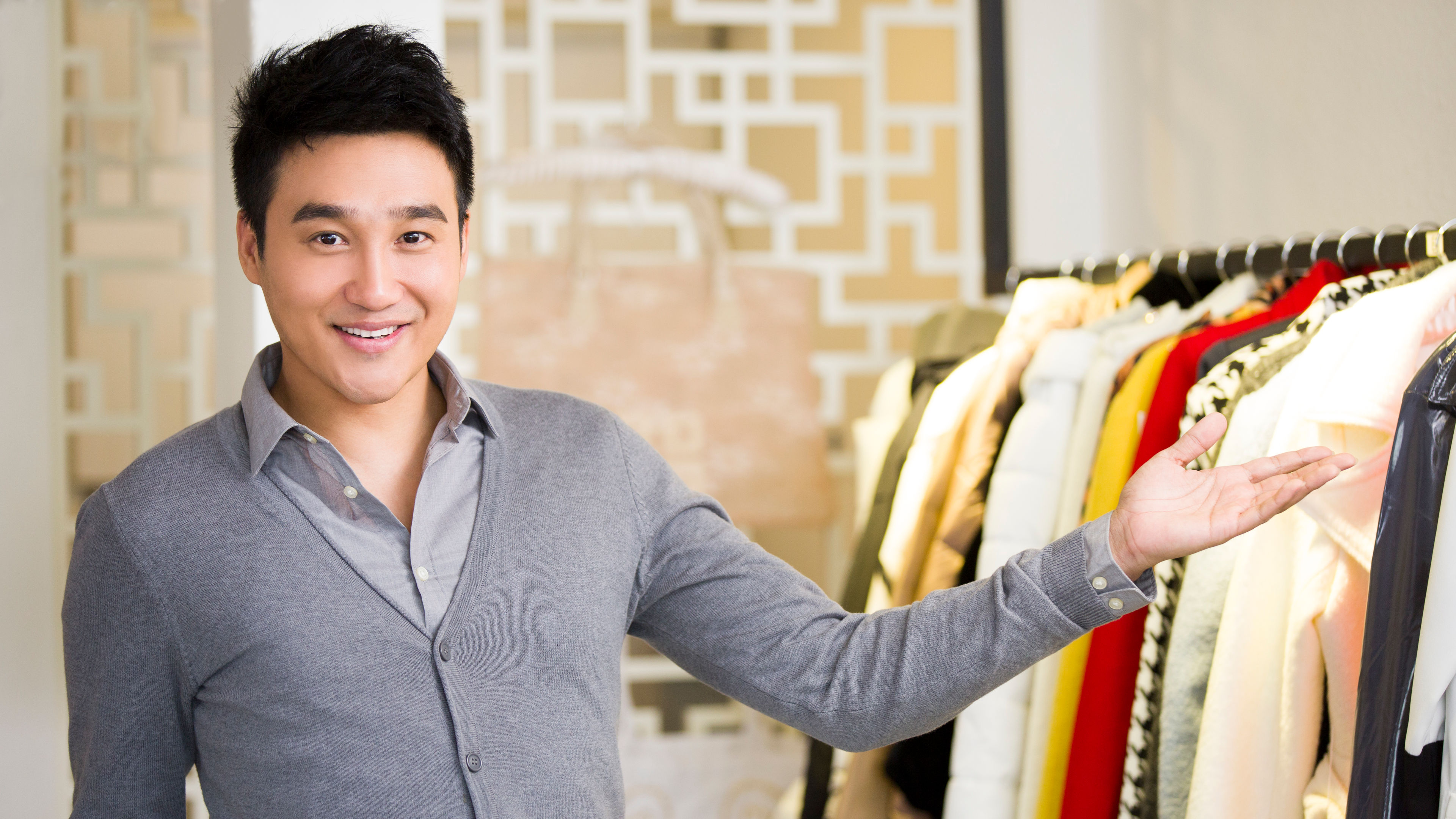 A friendly clothing store owner gesturing towards a beautifully organized rack of elegant garments 