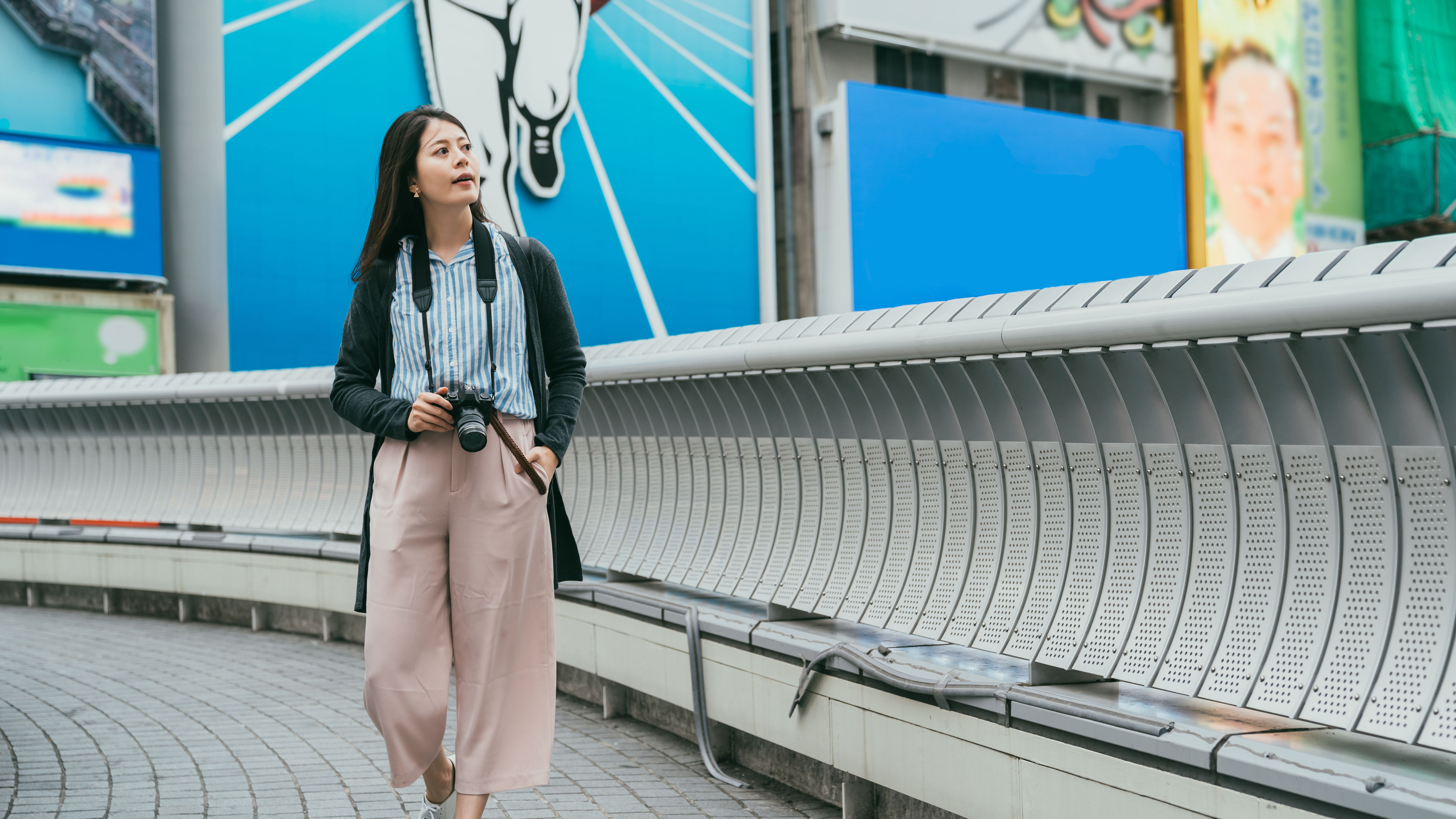 A woman walking in wide-leg pants with a camera
