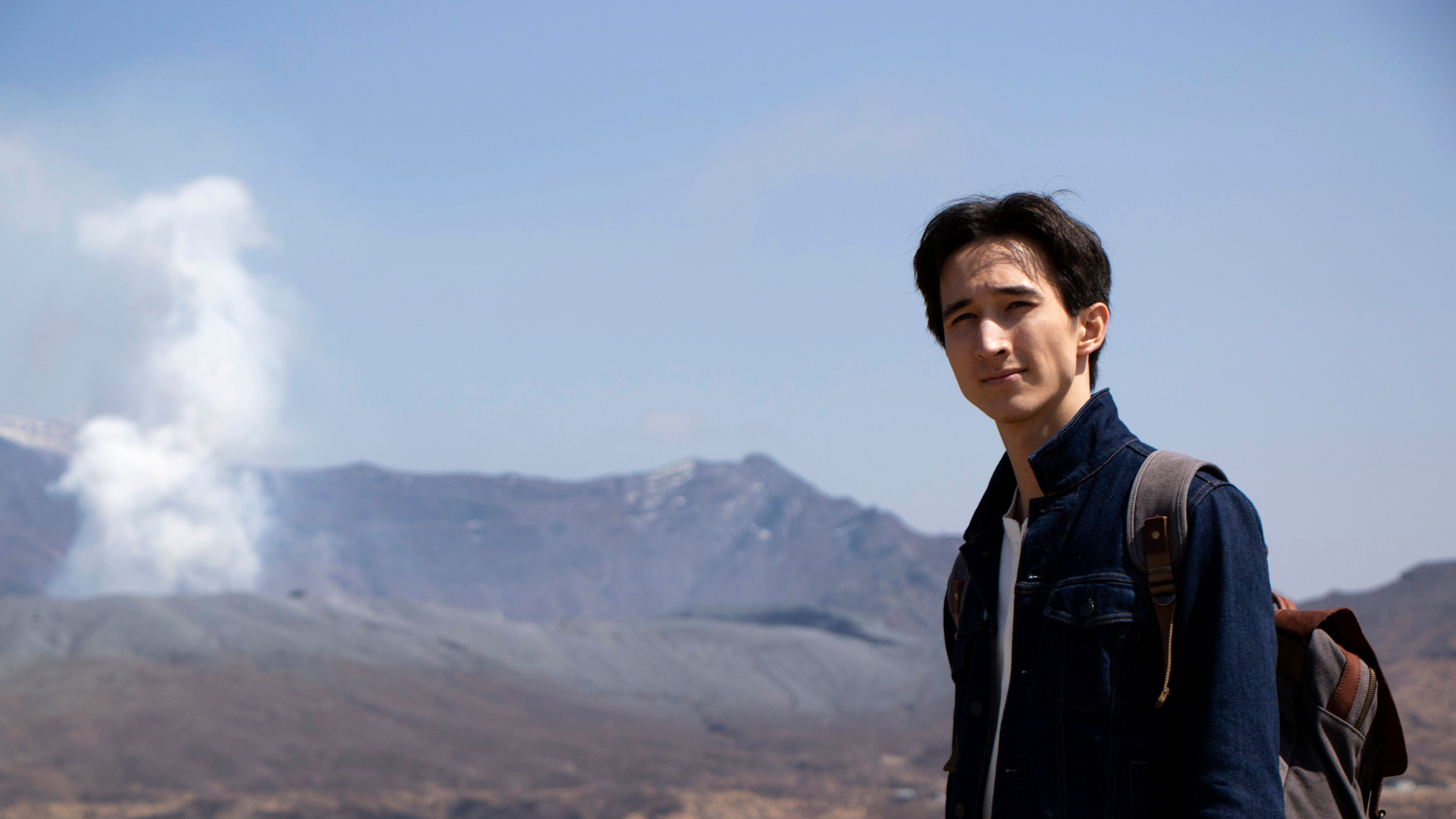 A young man stands in a scenic volcanic area