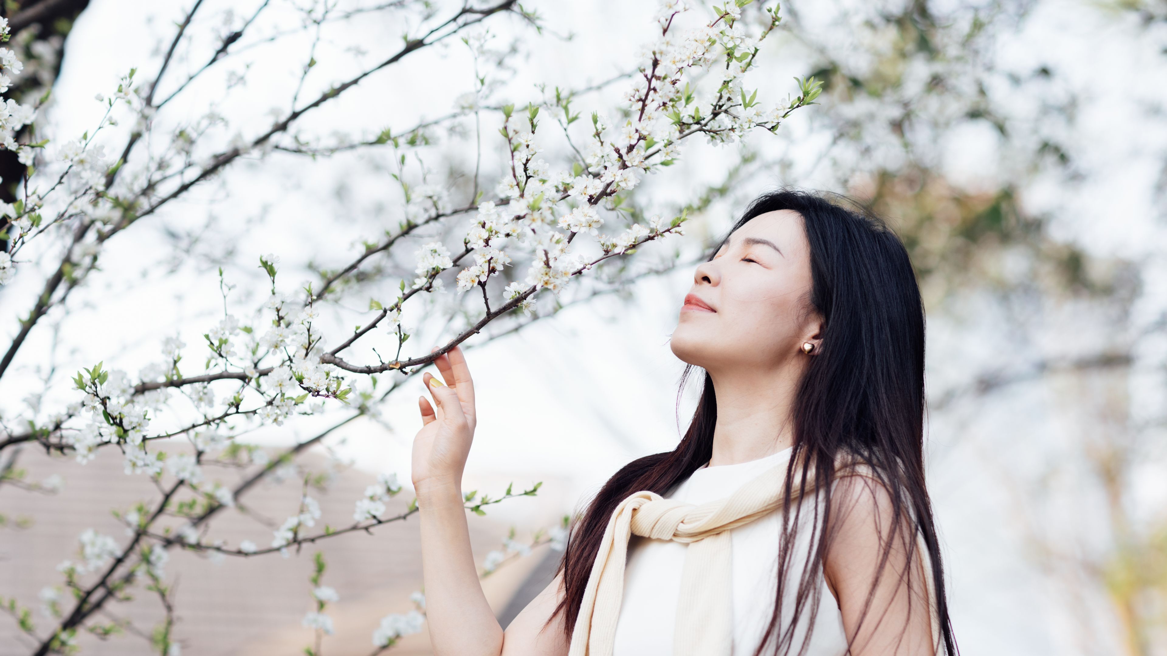 A young woman stands peacefully near a blossoming tree. 