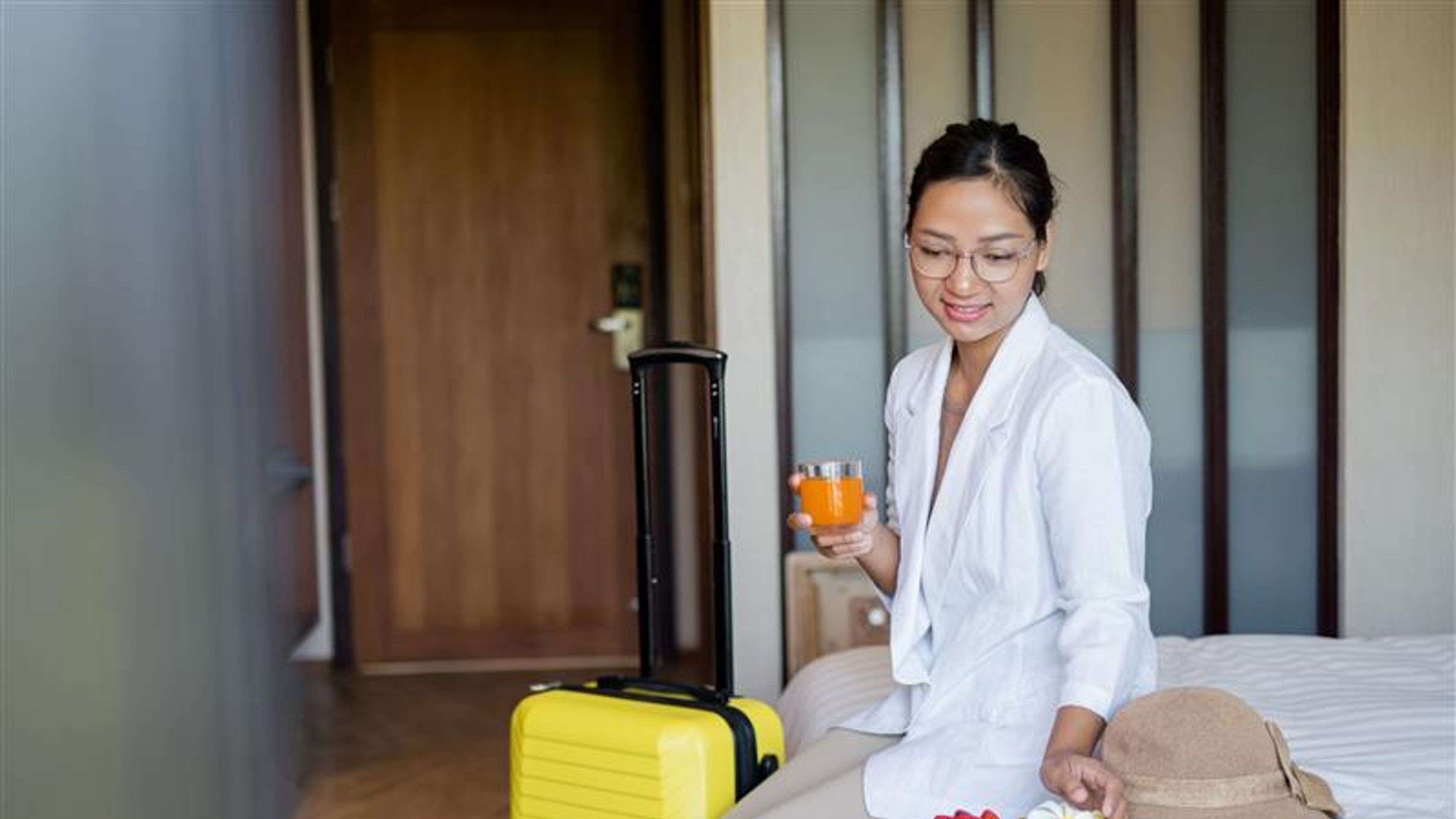 An Asian businesswoman sits on a bed in a hotel room