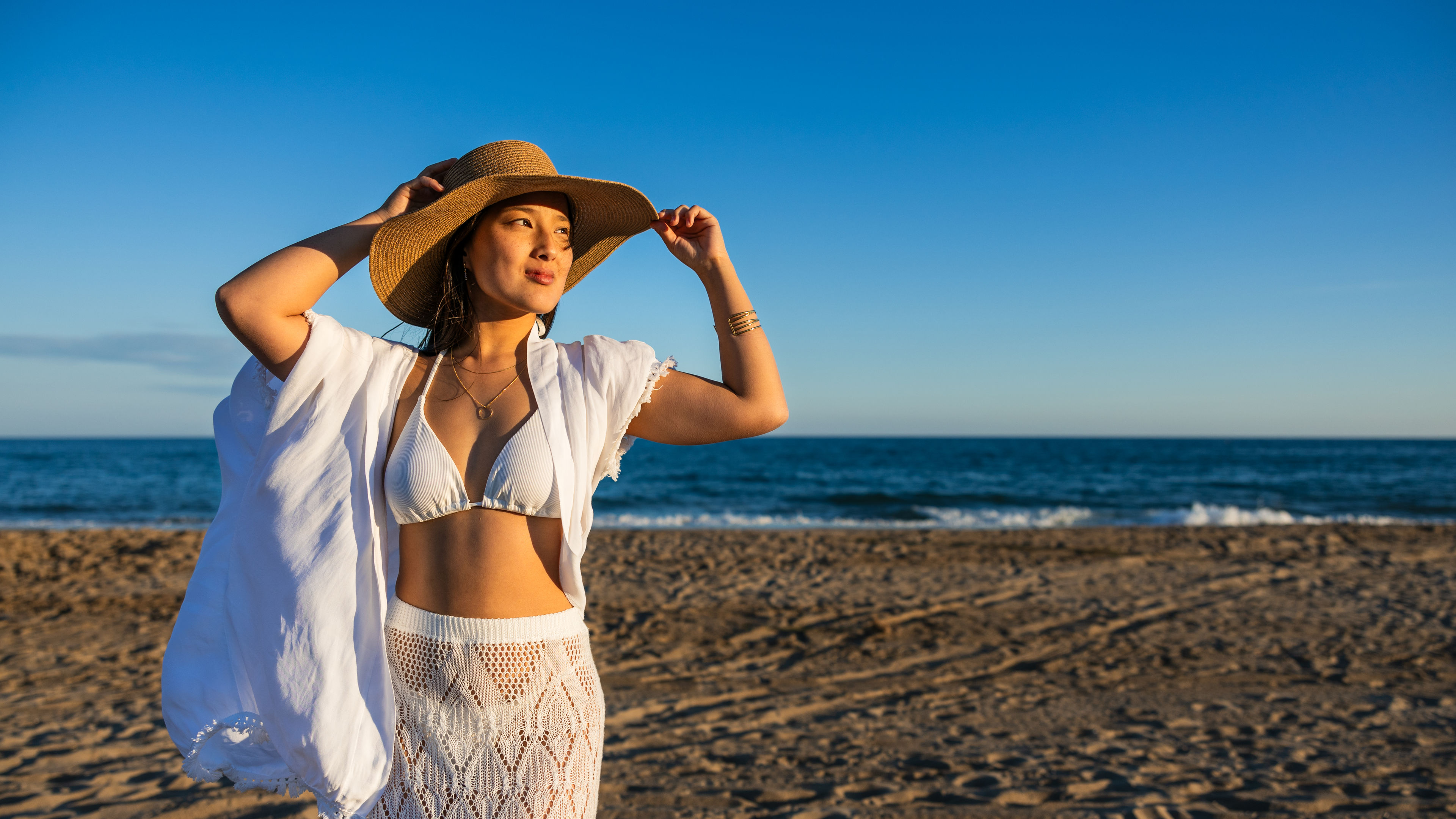 Asian woman walking along the beach at sunset.