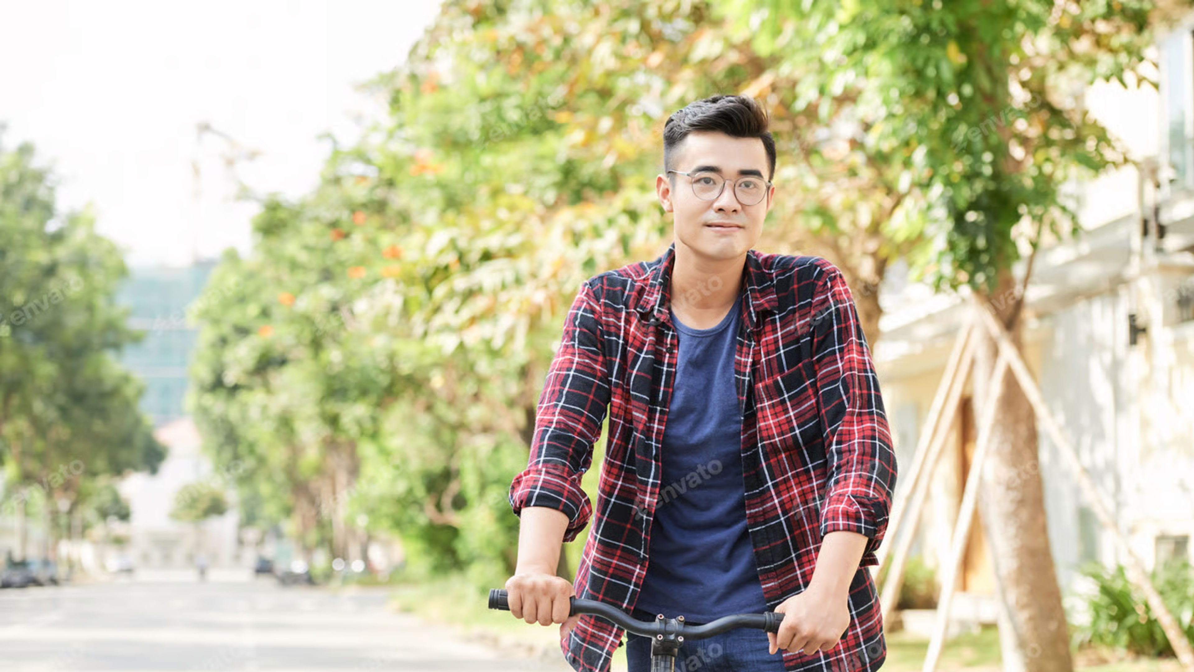 Positive young Asian man cycling in the street on sunny day 
