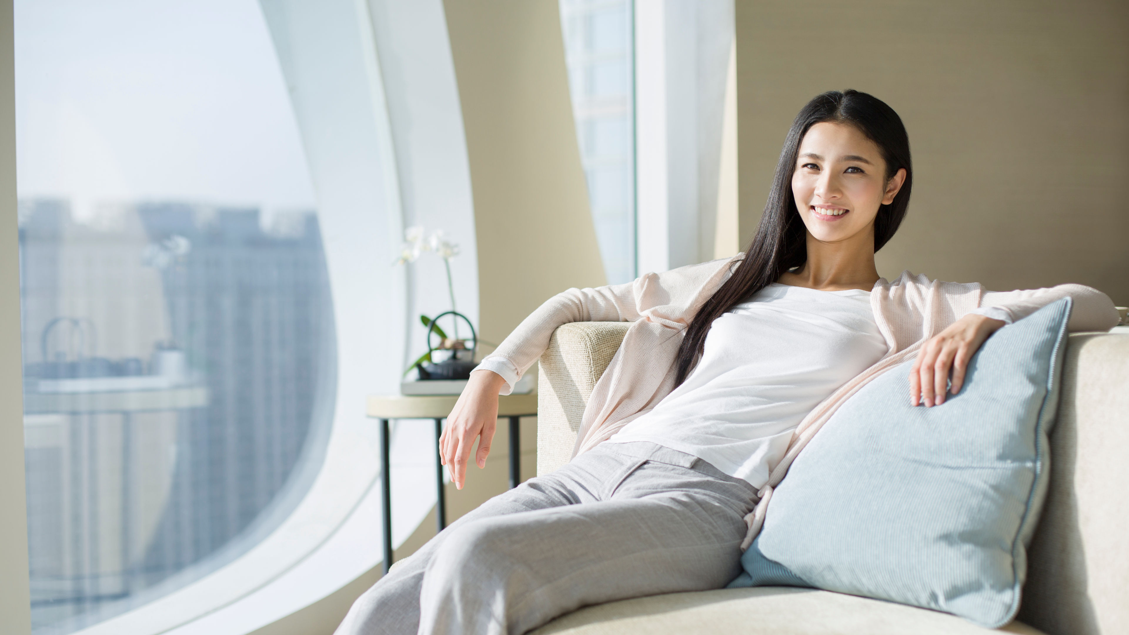 Happy young Chinese woman sitting on sofa