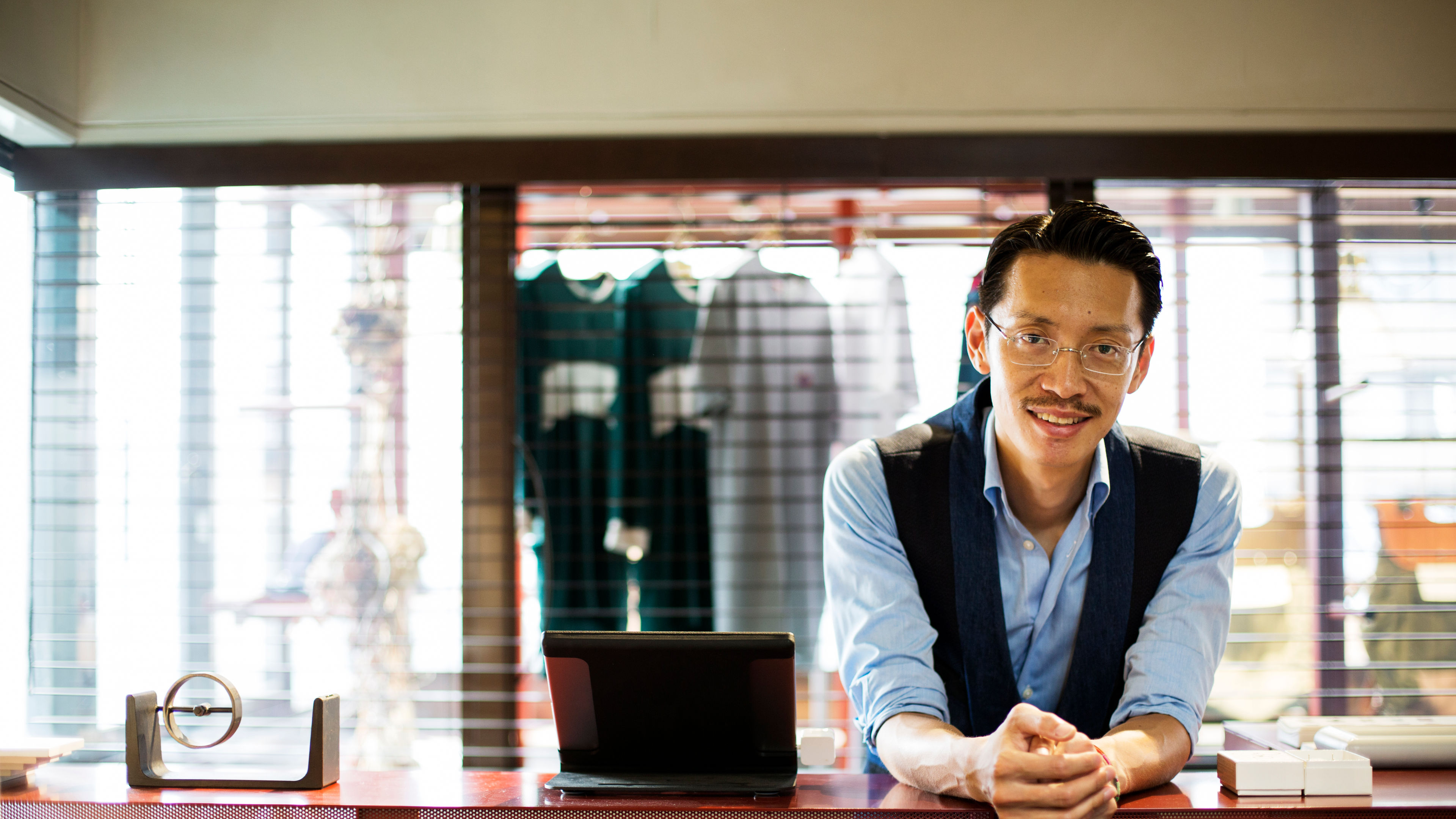 Japanese salesman standing at the counter in a clothing store, smiling at the camera