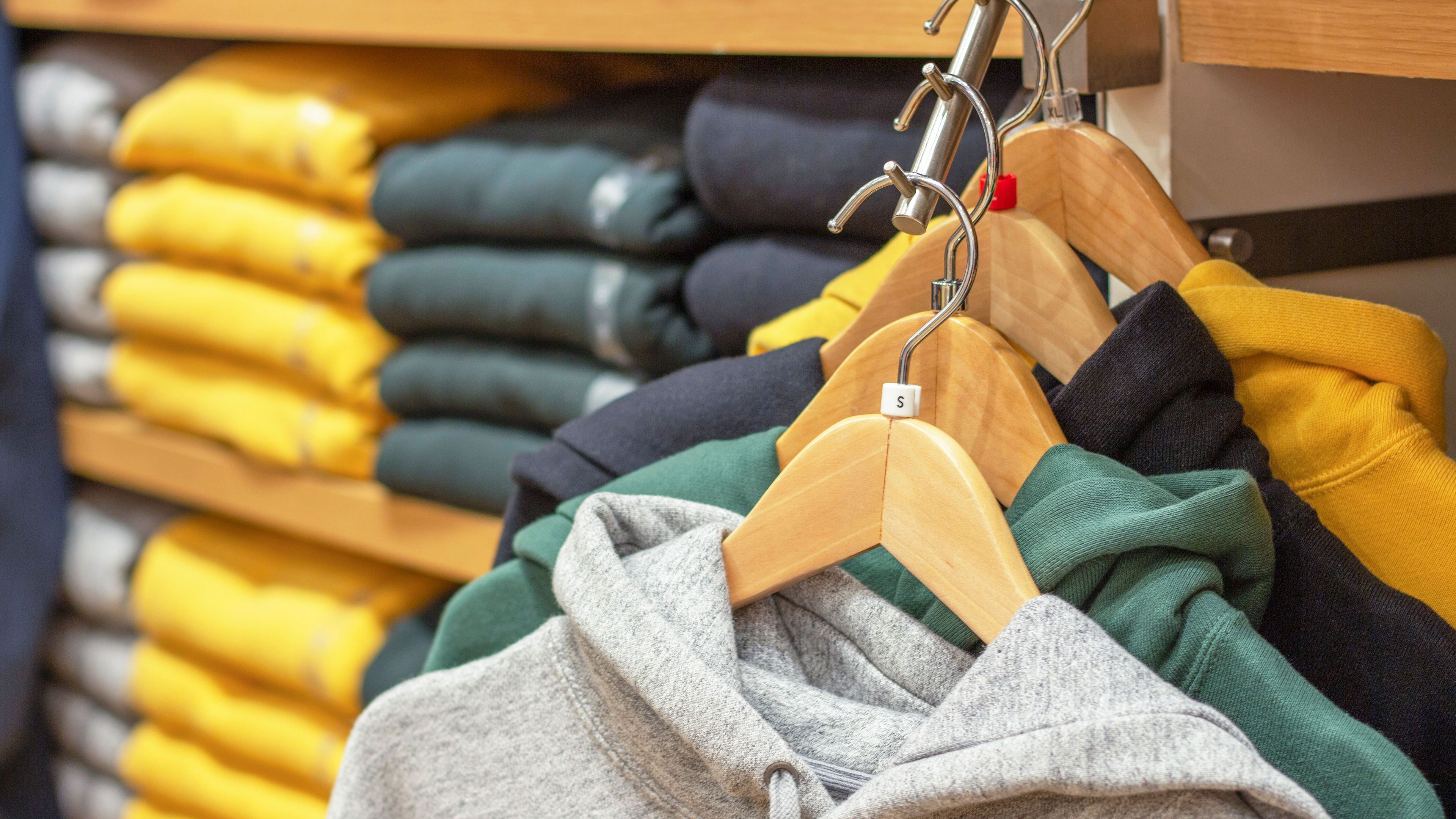 Multicolored hoodie hang on hangers against background of shelves with clothes in the store