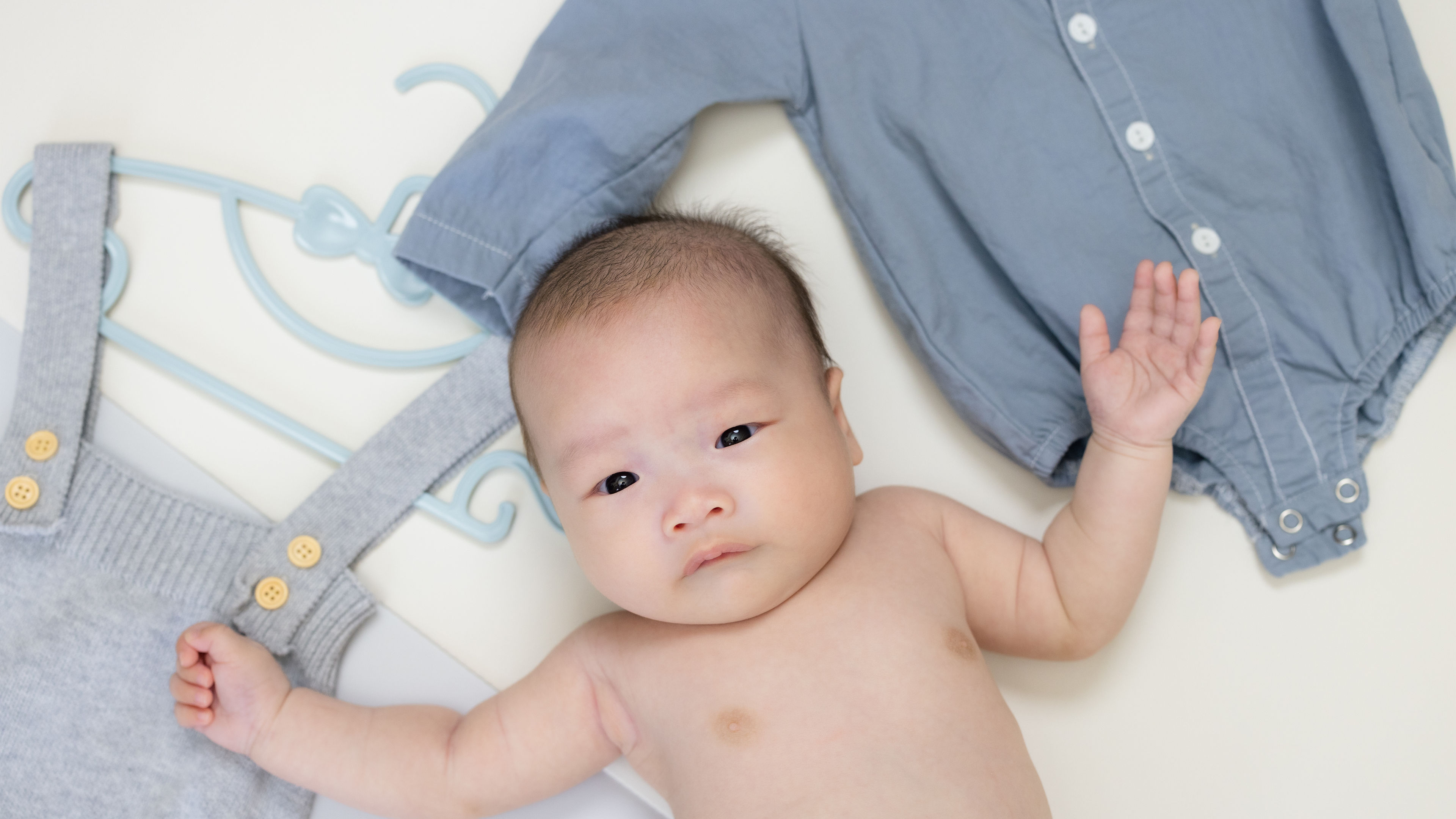 Newborn baby lying next to baby clothes