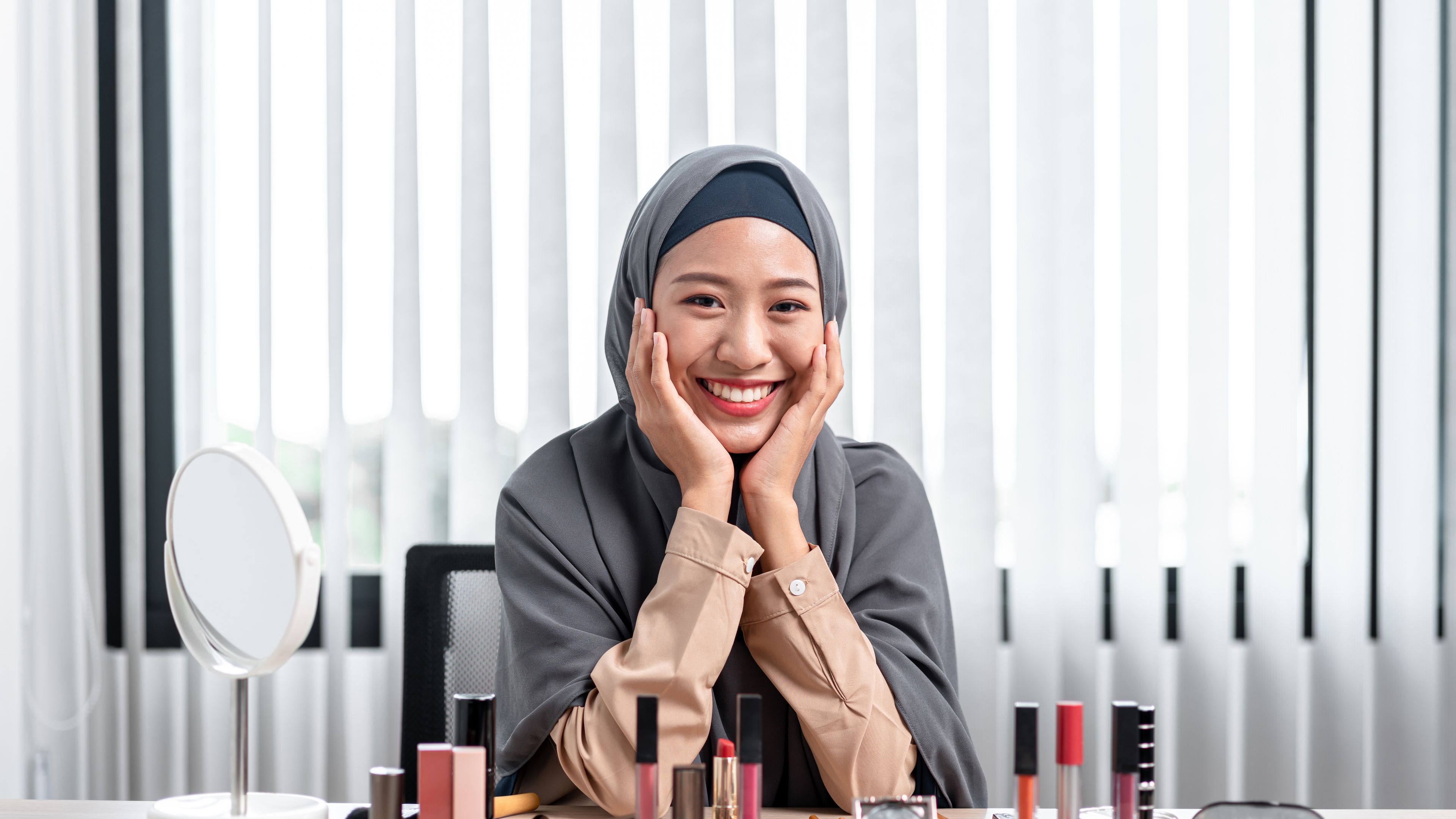 portrait of an Asian Muslim woman looking at a camera and smiling while teaching a makeup tutorial online live 