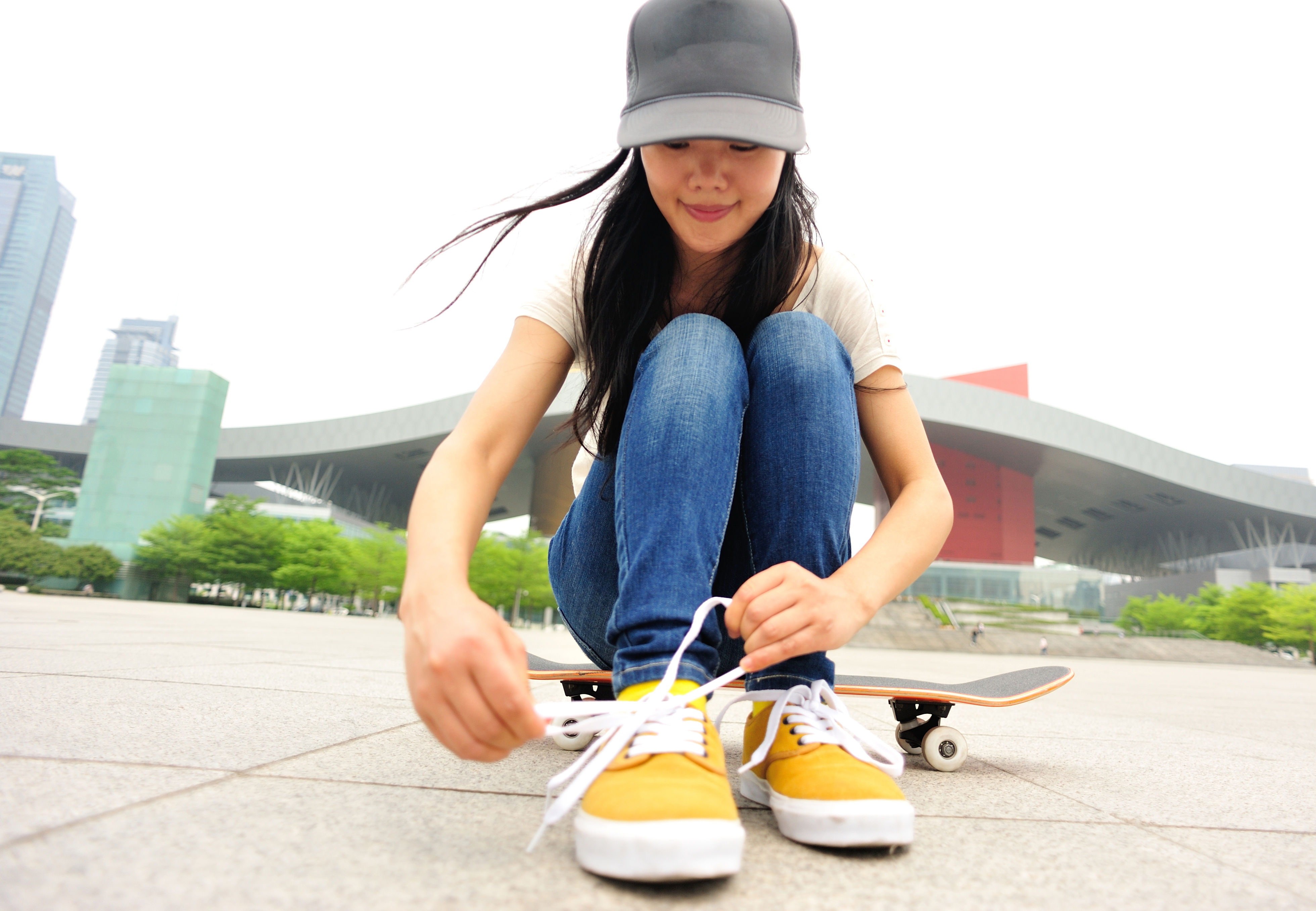 A skateboarder ties the laces of bright yellow sneakers while sitting on a sidewalk.  