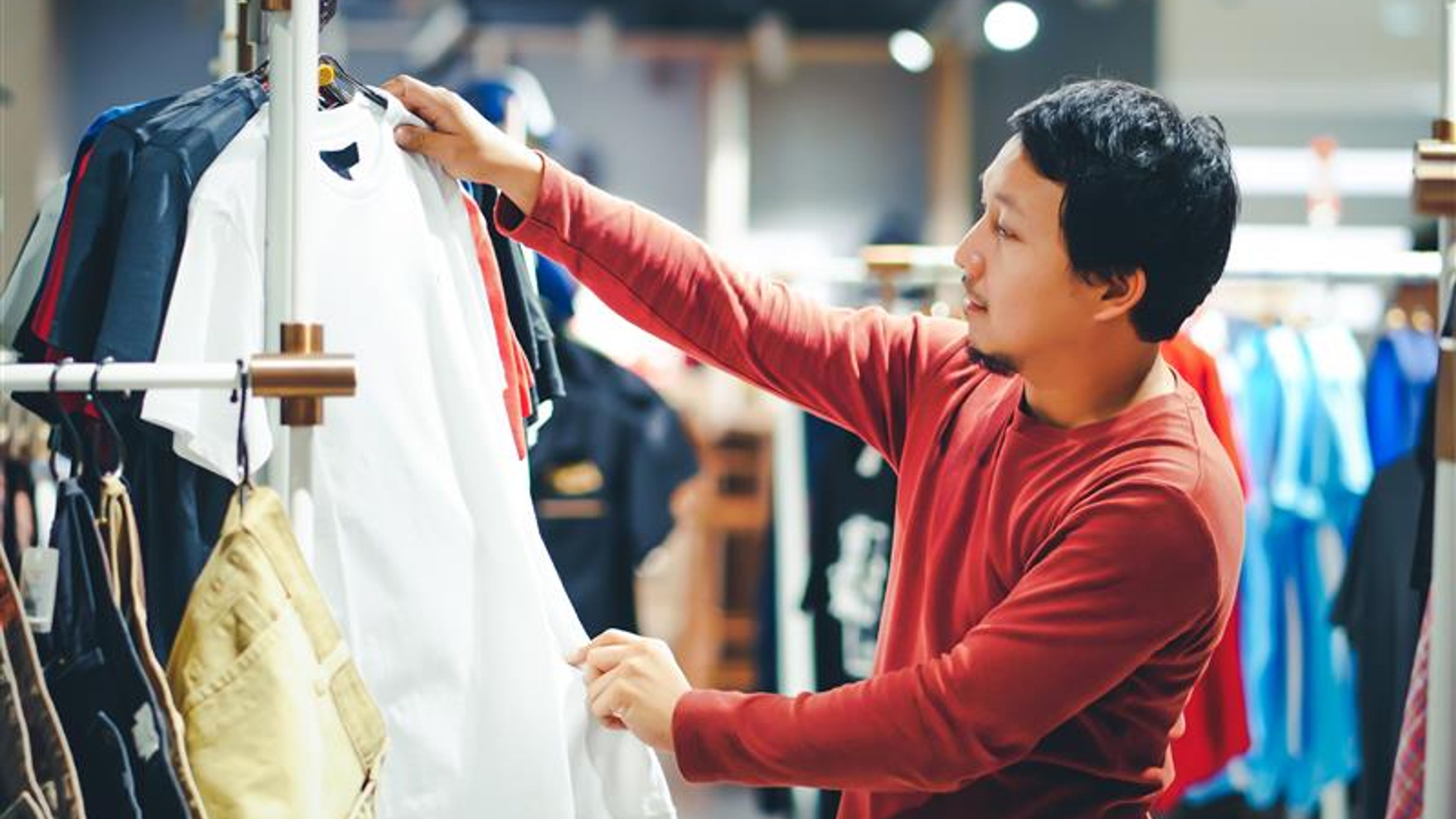 Smart man with beard choosing clothes in clothing store at shopping centre