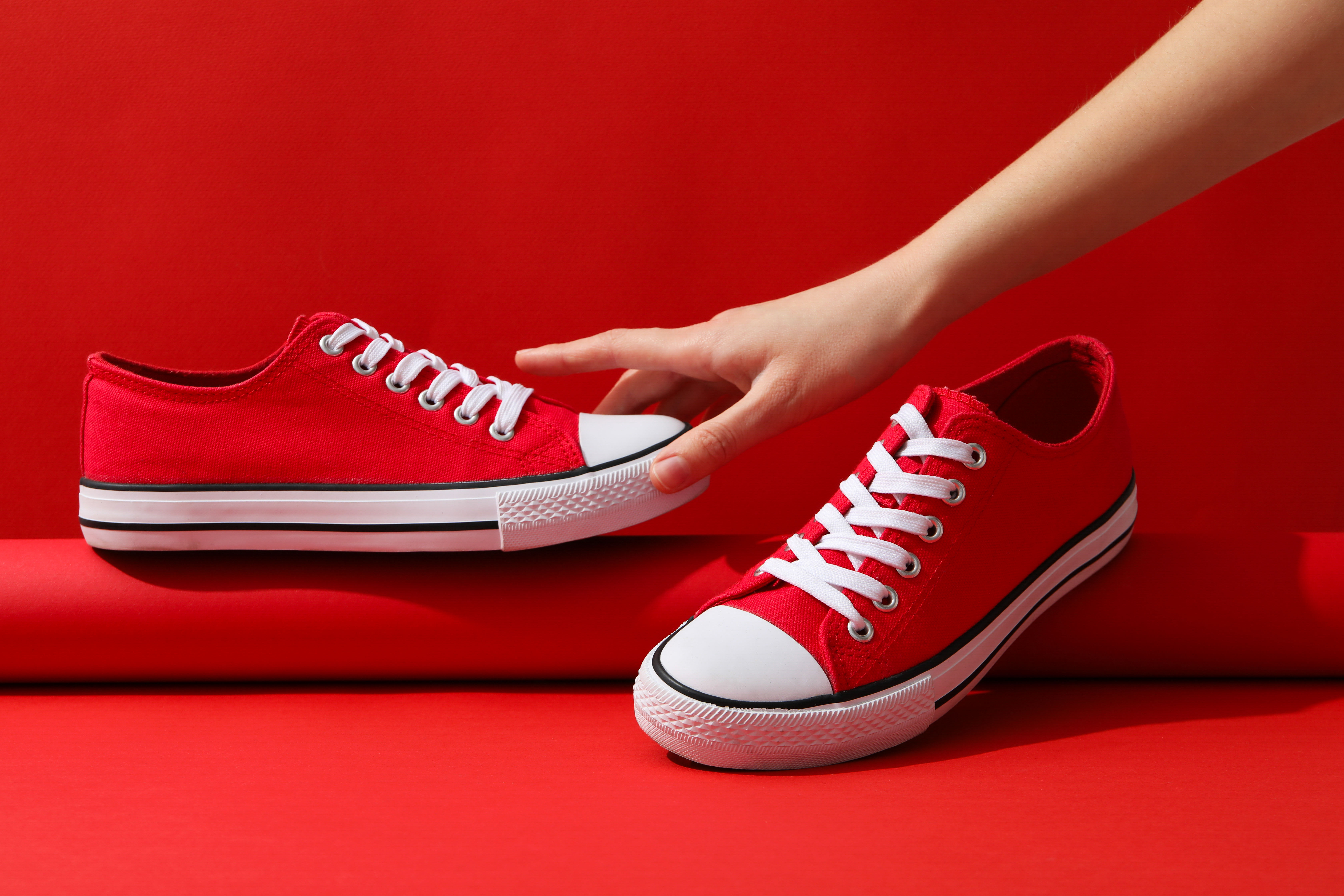 A pair of vibrant red sneakers is displayed on a red background 
