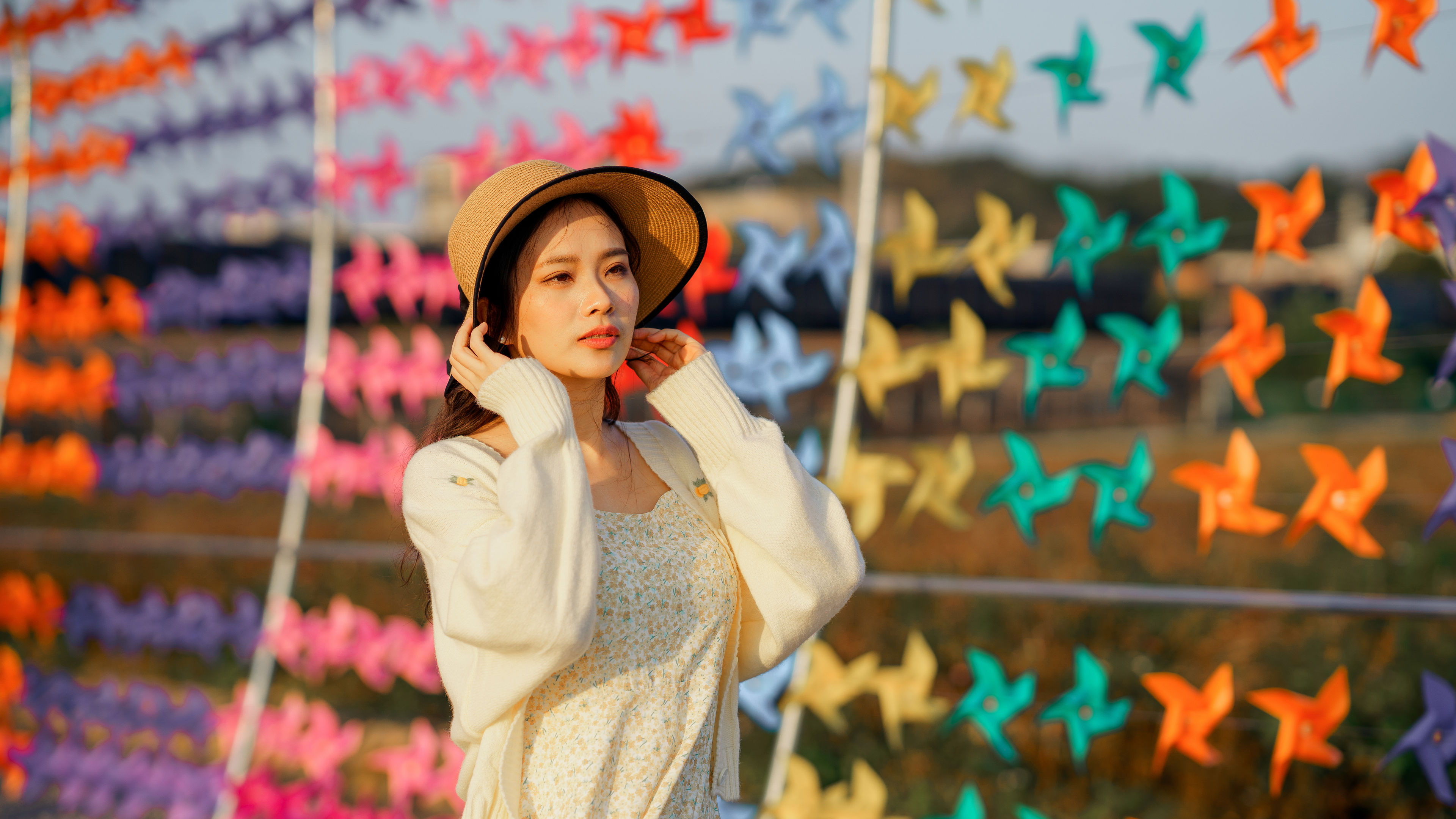 Asian girl in a dress and hat by colourful pinwheels. 