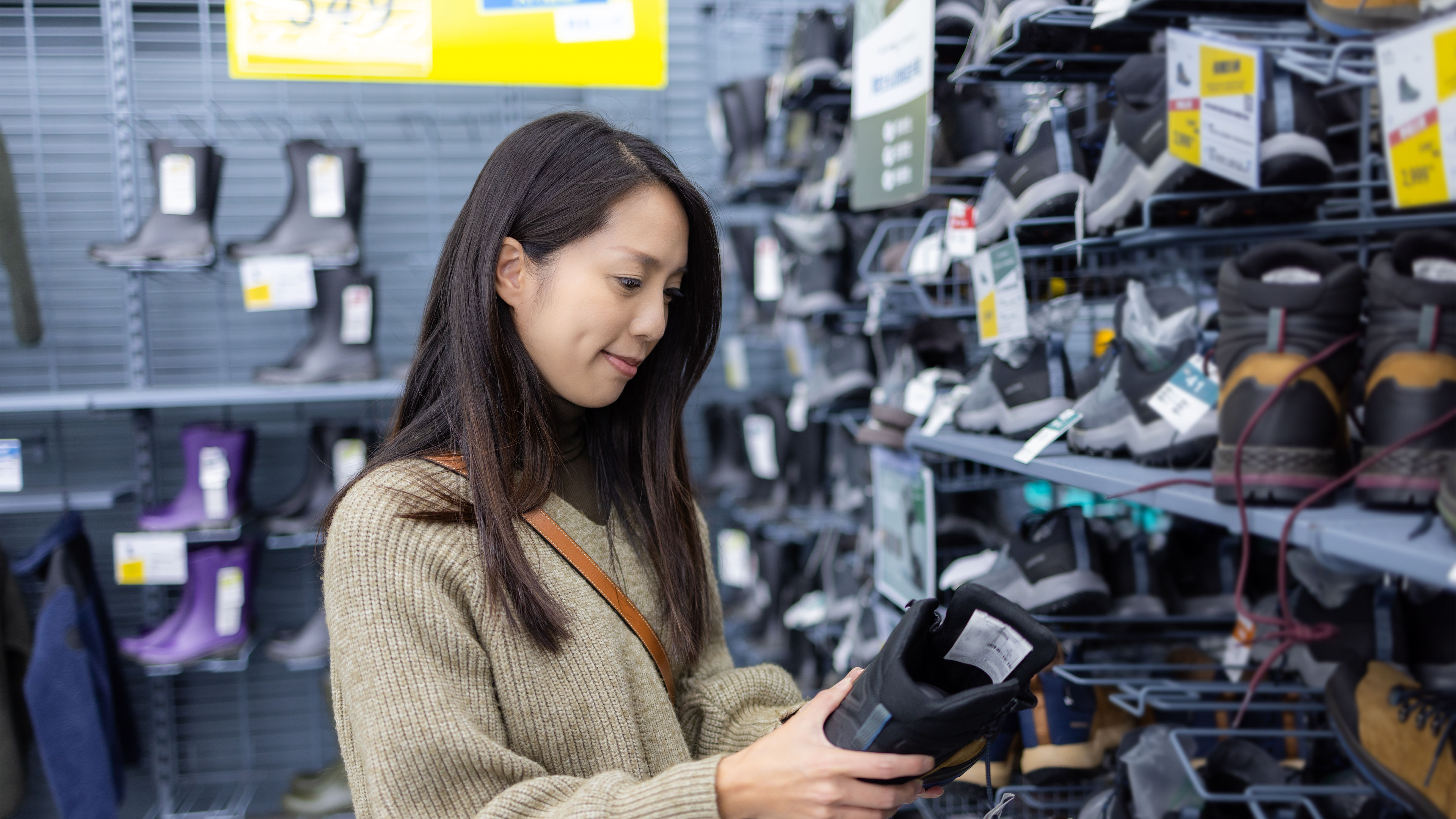 A woman in a cozy sweater examines a black winter boot in a shoe store 
