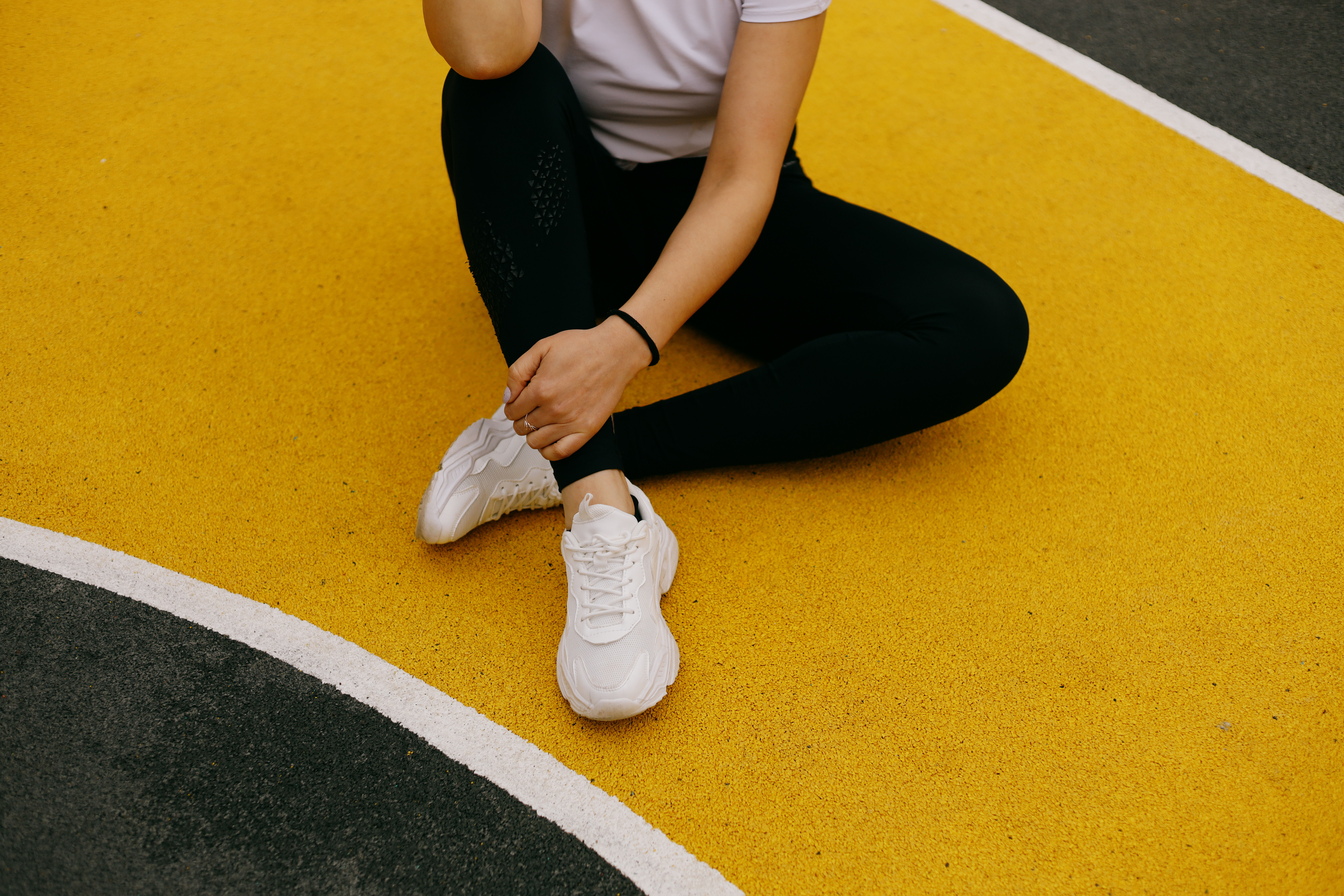 A person is sitting on a yellow and black court wearing white sneakers and black leggings, 
