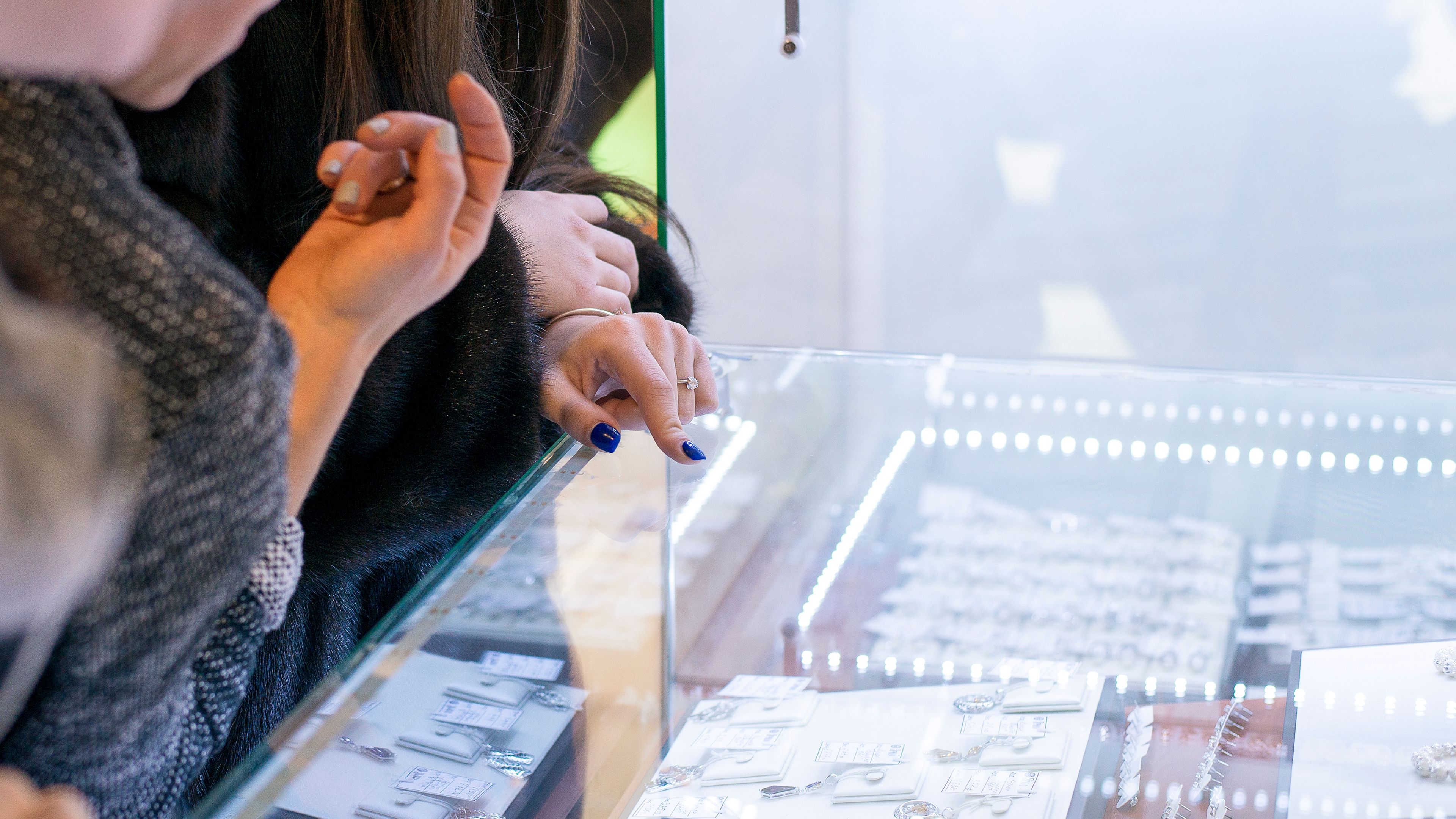 A group of women closely examining a jewelry display case filled with glittering pieces 