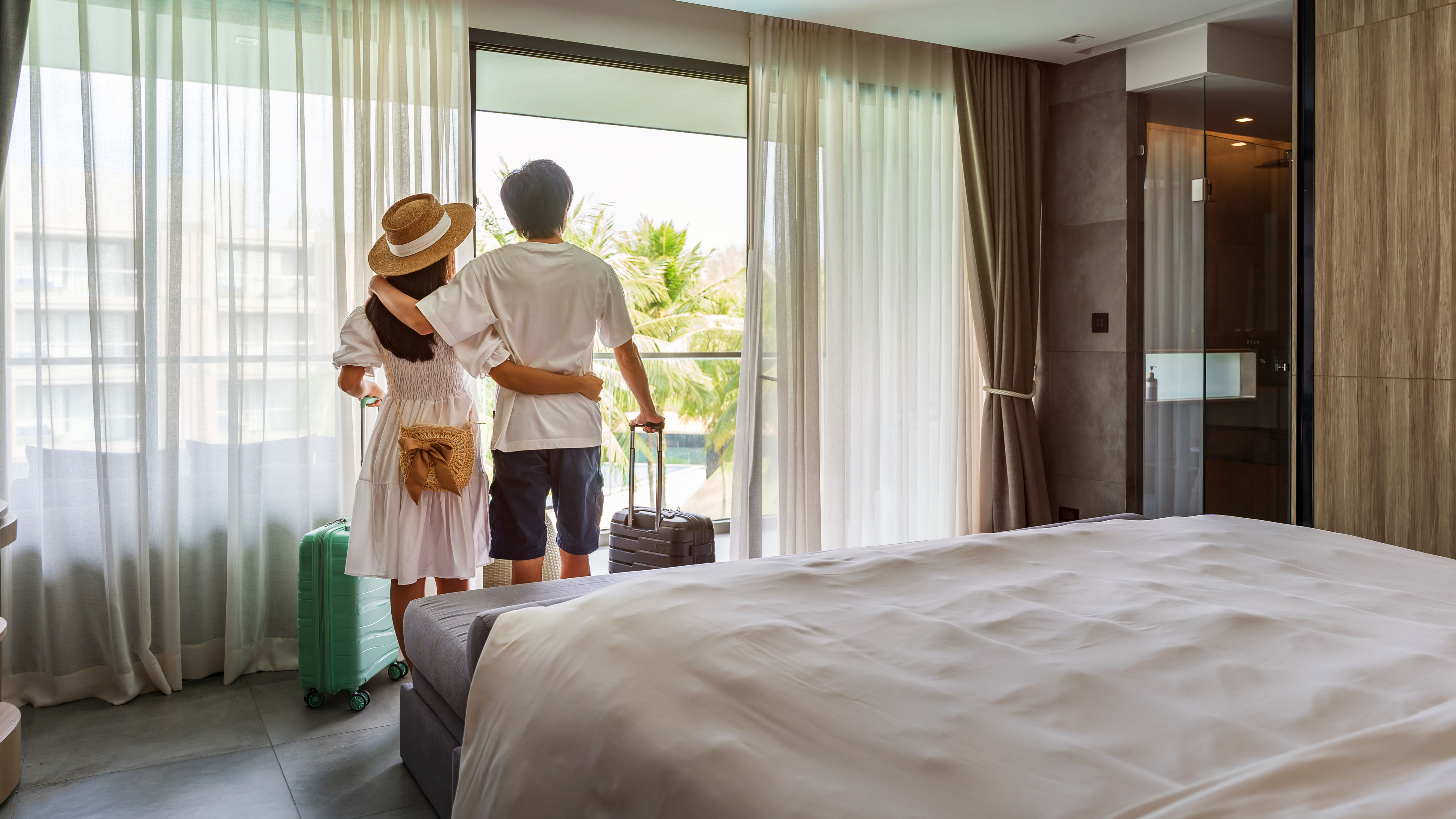 Young couple traveler opening the curtains and looking at the view from the window of a hotel room